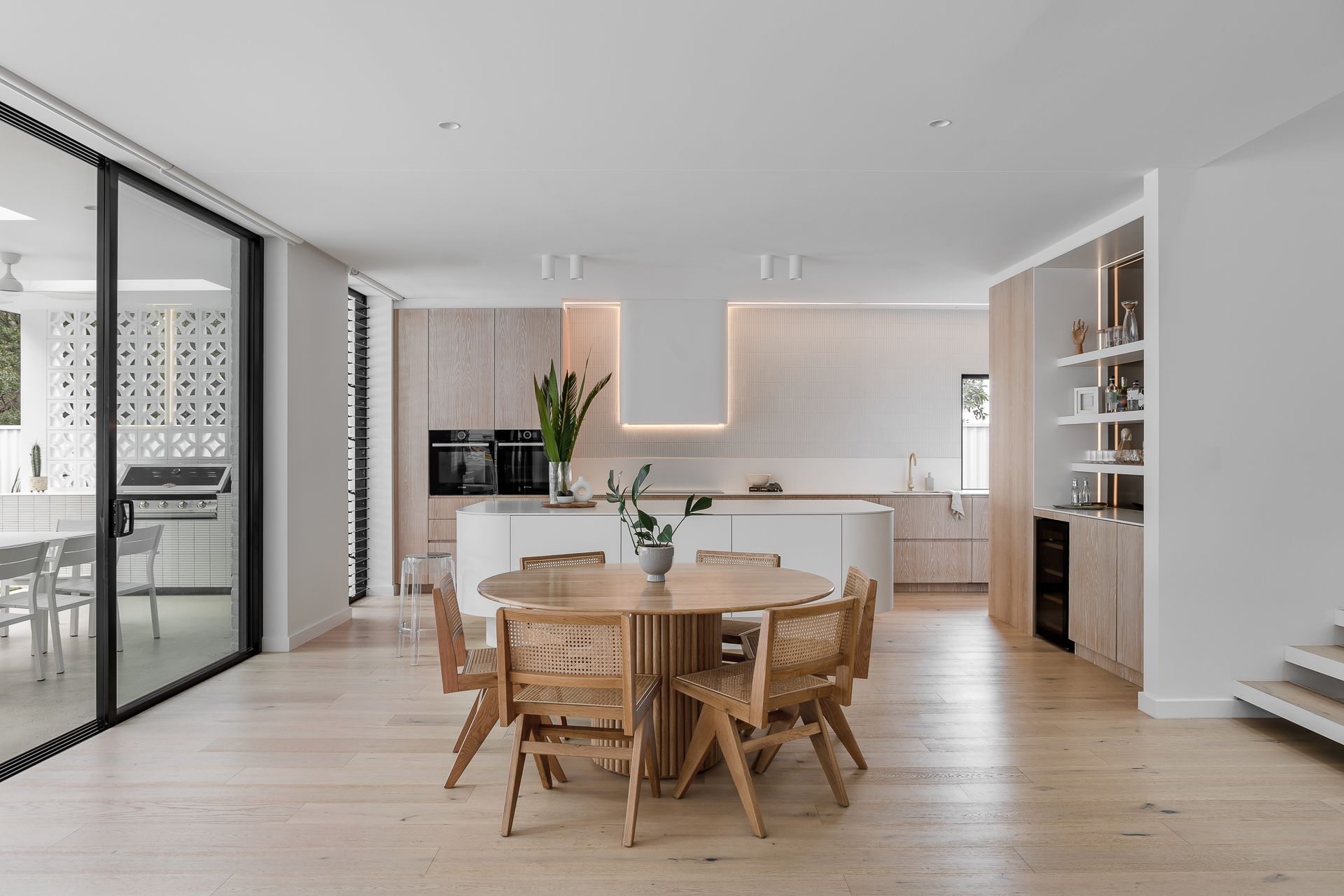 Modern kitchen with light wood cabinets, round table, woven chairs, and sliding glass doors — Escarpment Building in Austinmer, NSW