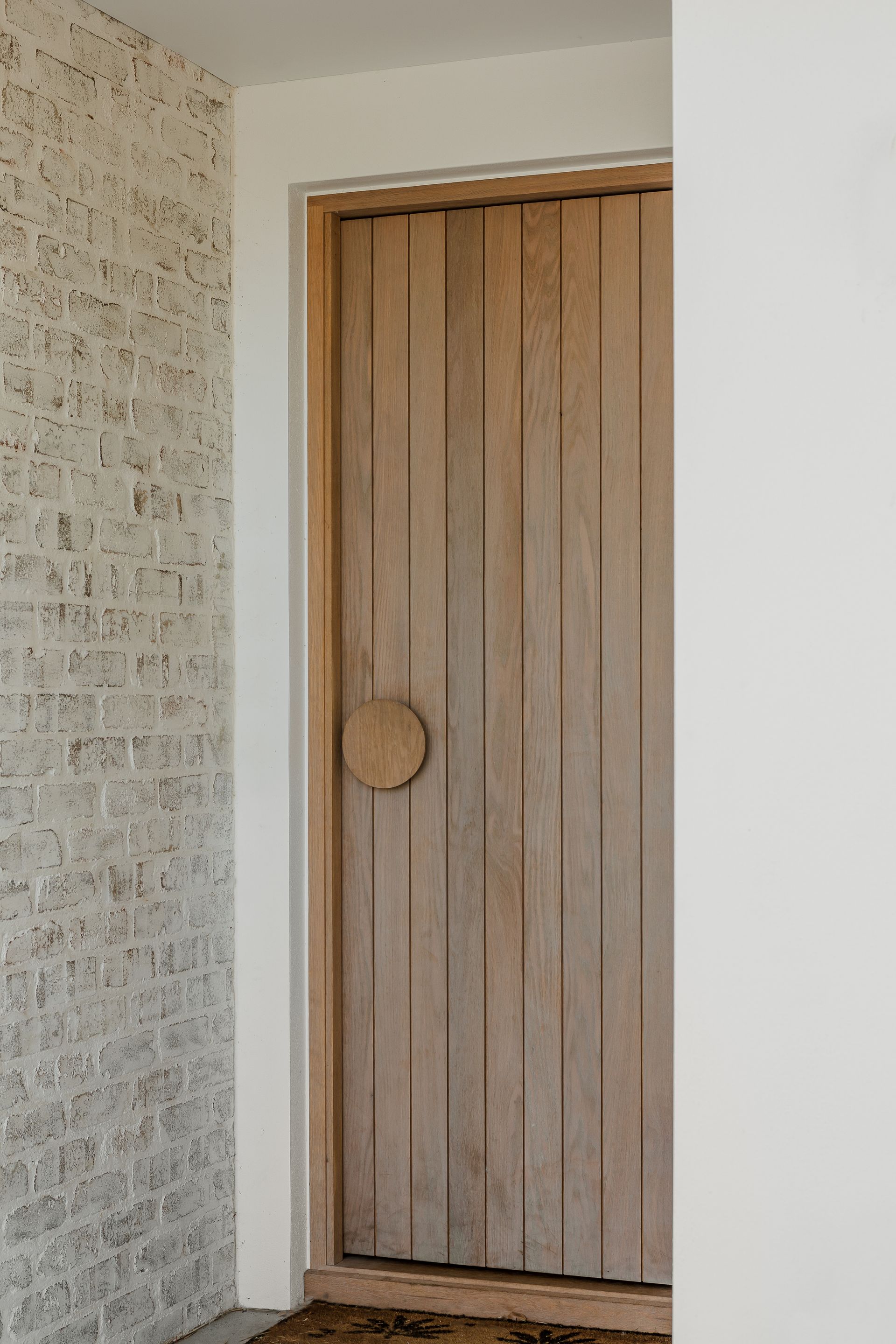 Wooden door with vertical panels and a round handle set in a white door frame between white brick and a white wall — Escarpment Building in Austinmer, NSW