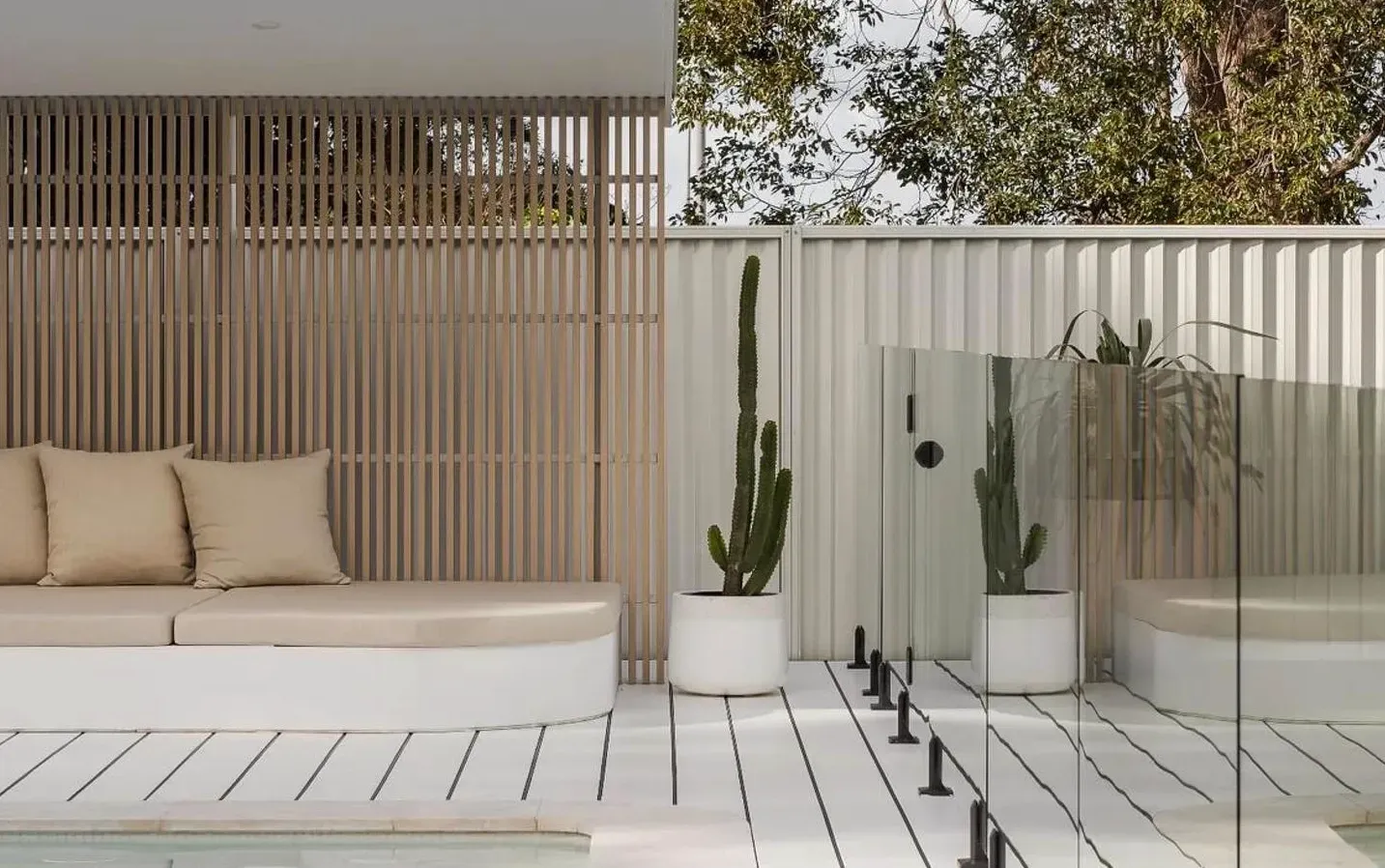 Outdoor seating area with beige cushions, vertical wooden screen, white deck, and cacti — Escarpment Building in Austinmer, NSW