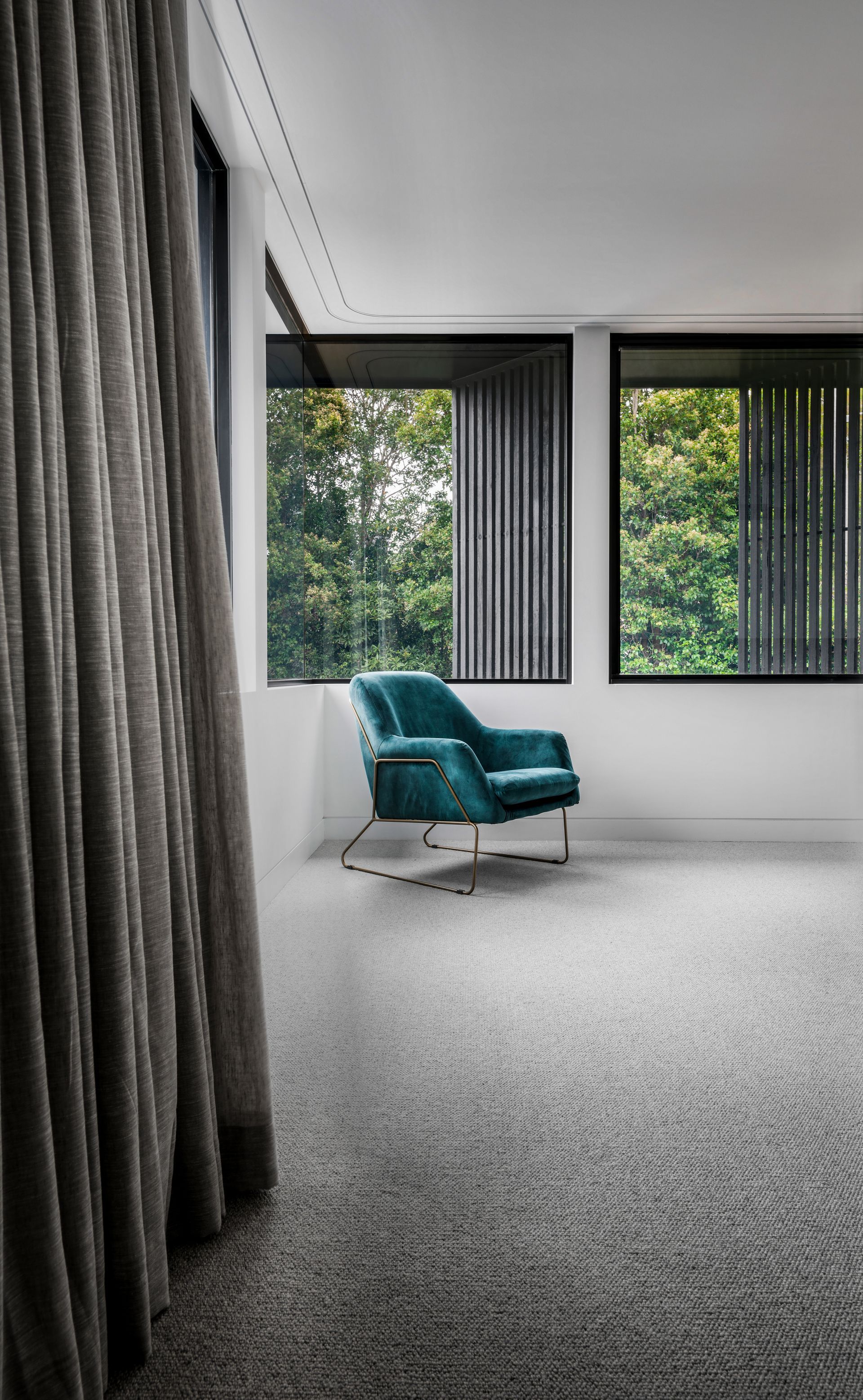 Teal velvet armchair in a minimalist room with large windows, gray carpet, and sheer curtains — Escarpment Building in Austinmer, NSW