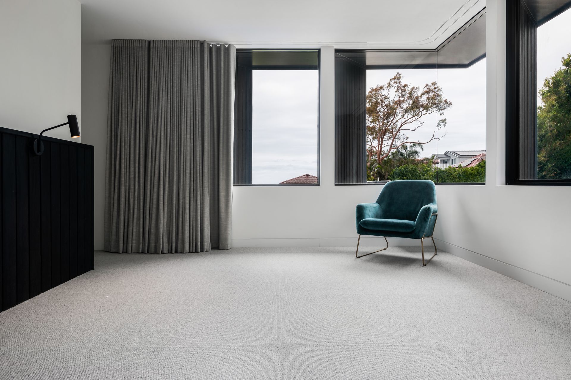 Empty room with gray carpet, a teal armchair, and a dark curtain next to a window with an outdoor view — Escarpment Building in Austinmer, NSW
