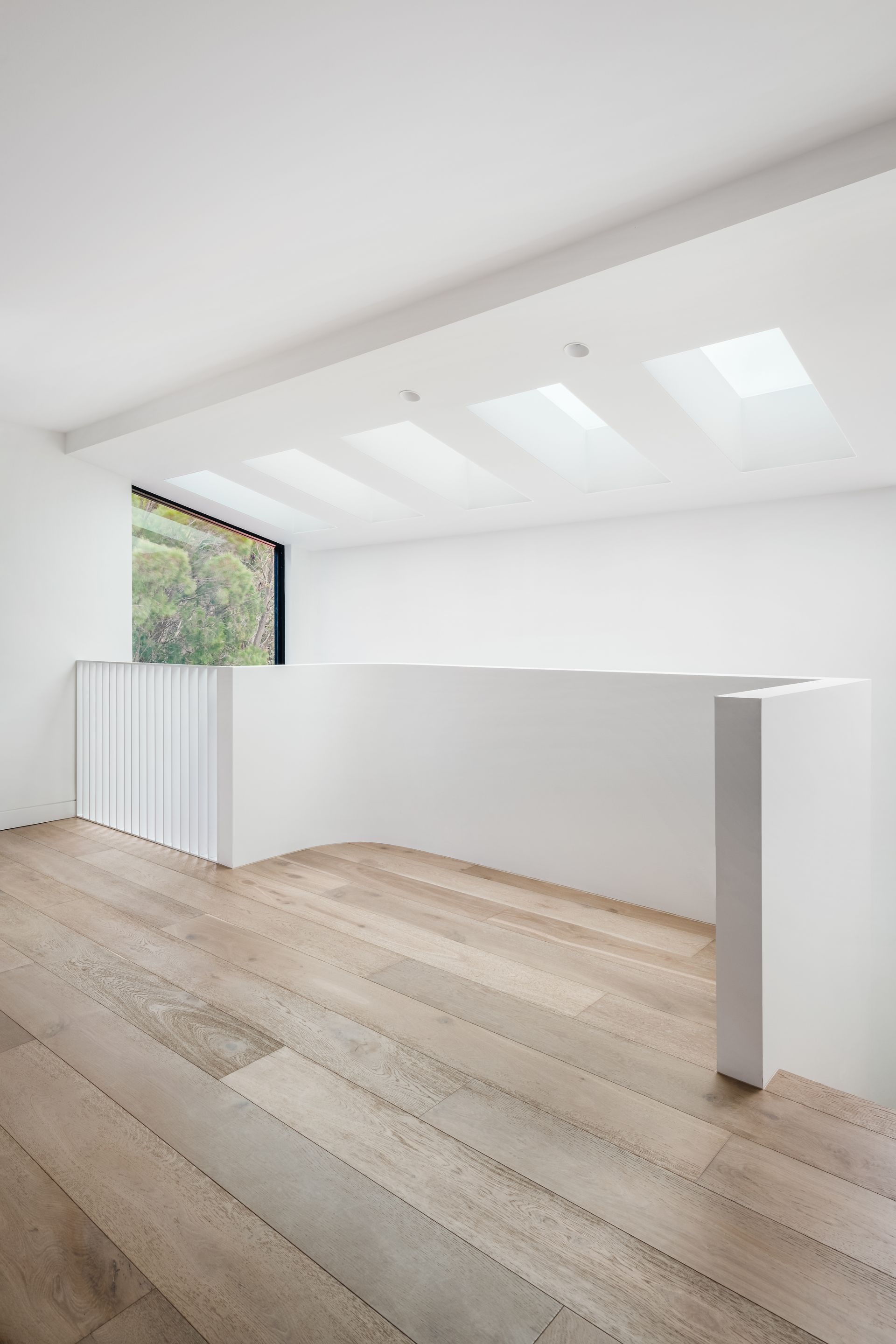 Interior with light wood floor, white walls and railing, large window, skylights — Escarpment Building in Austinmer, NSW