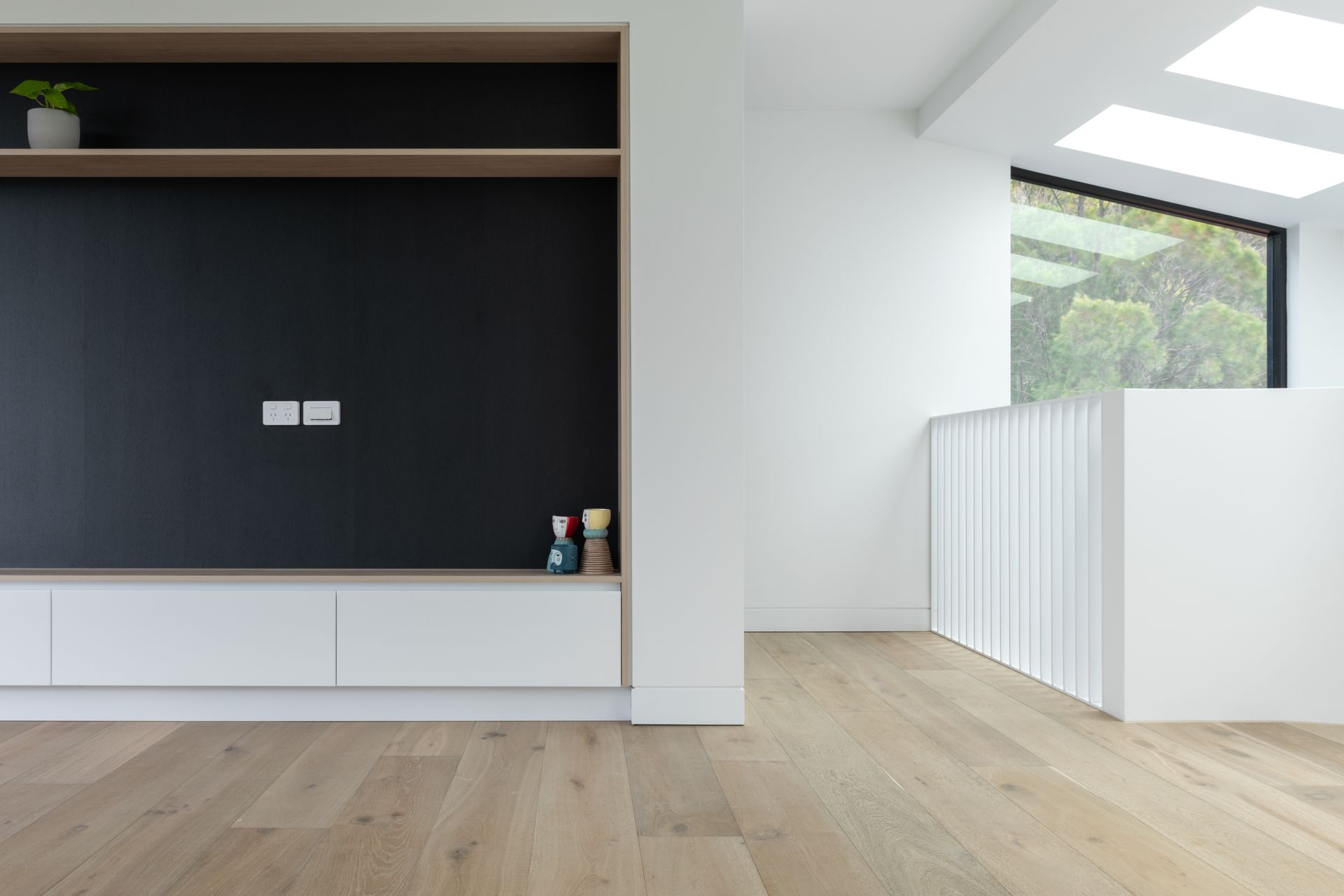Modern interior with wooden floors, black accent wall, and white cabinetry. Skylight and minimalist staircase visible — Escarpment Building in Austinmer, NSW