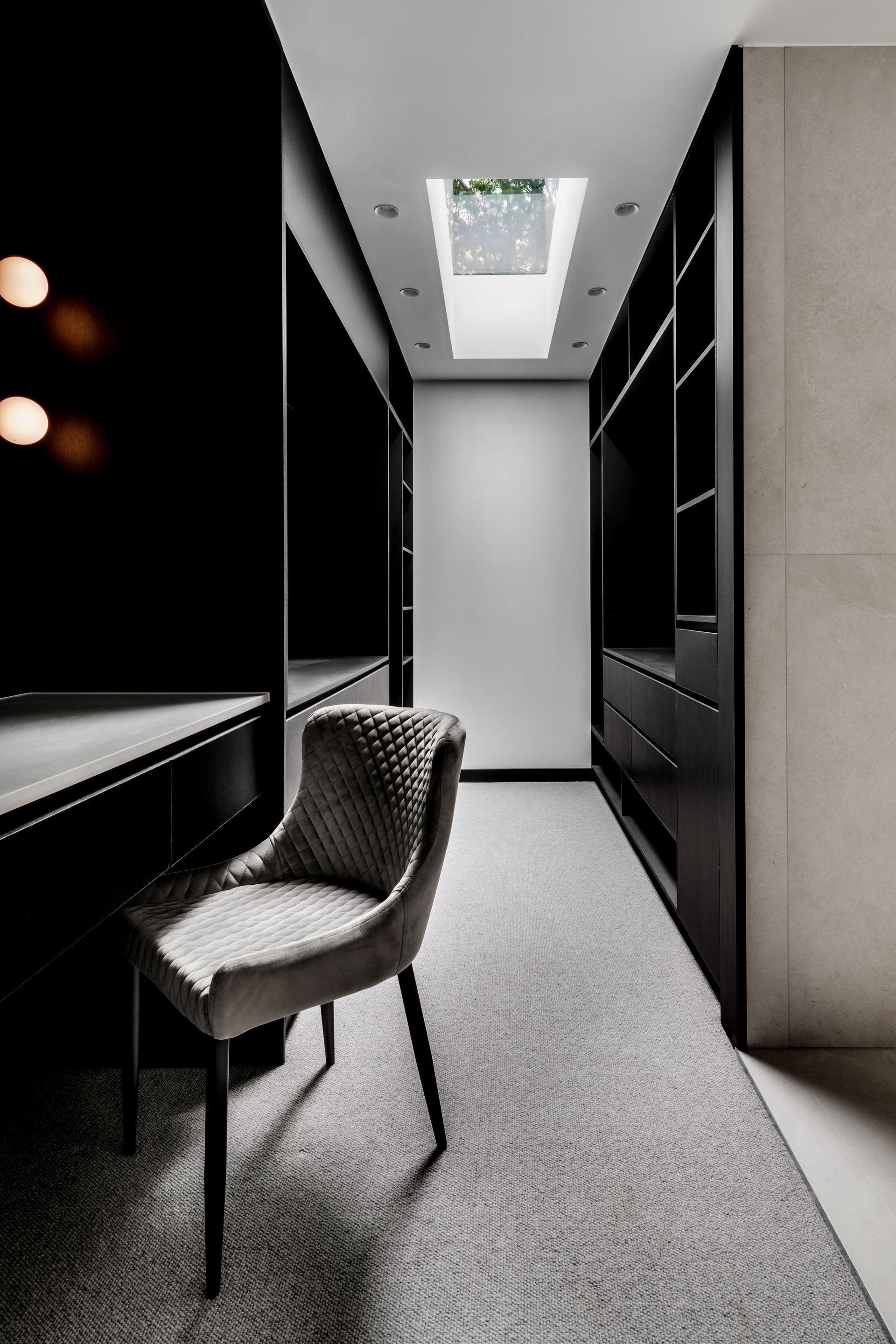 Narrow, modern closet with black cabinetry, desk, light-colored chair, and a skylight — Escarpment Building in Austinmer, NSW