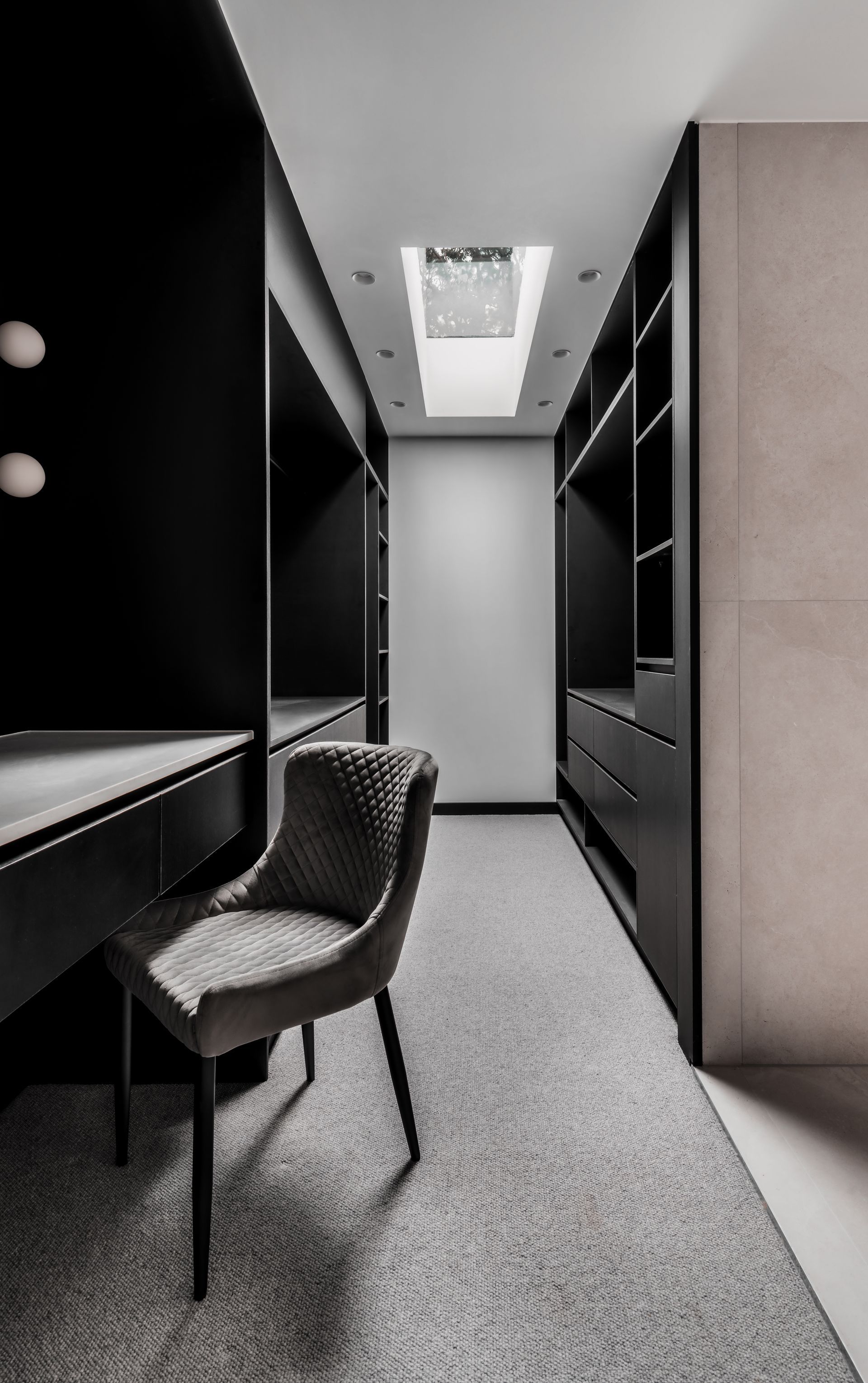 Narrow, black-walled walk-in closet with built-in shelving and desk, carpeted floor, and gray upholstered chair — Escarpment Building in Austinmer, NSW