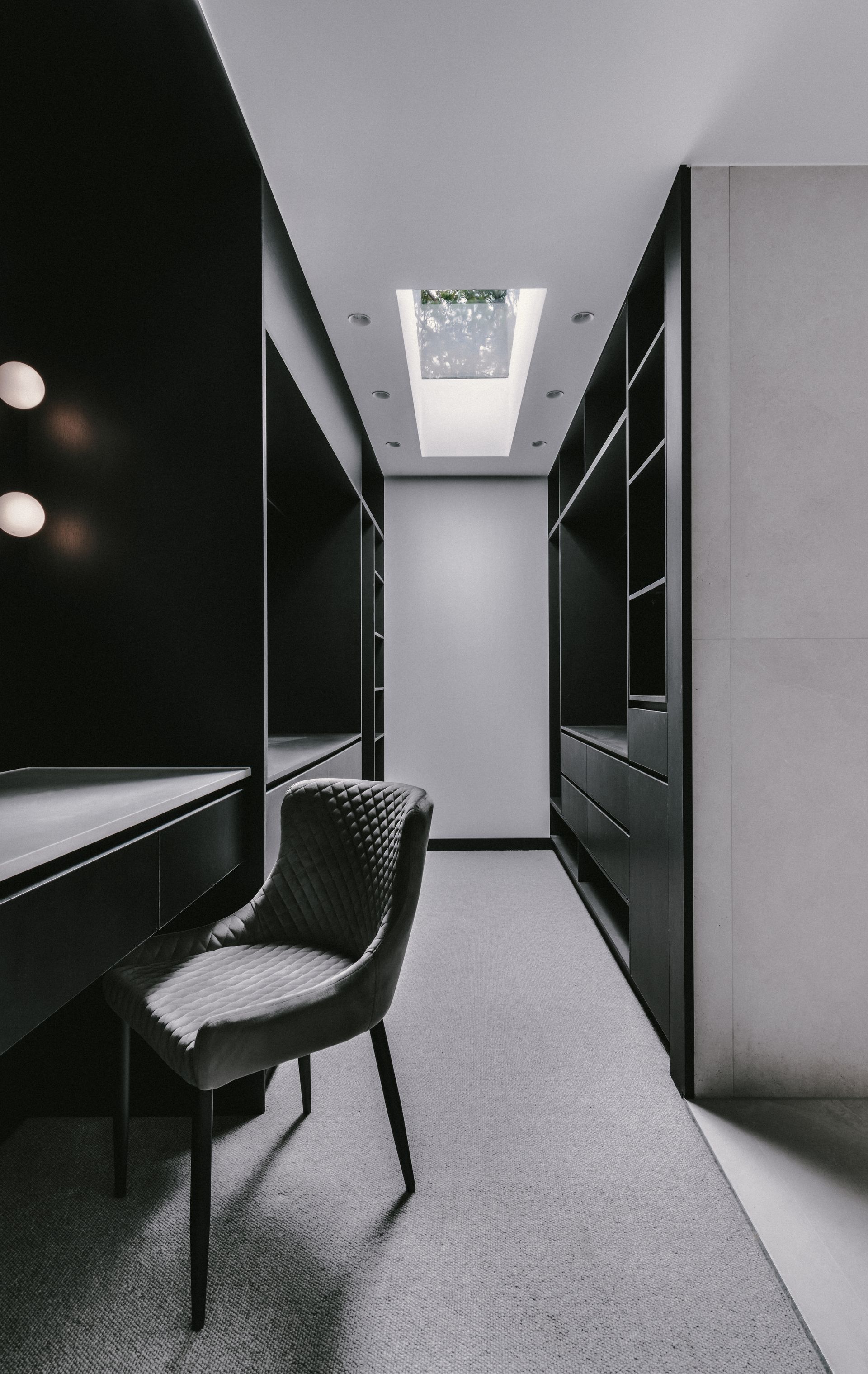Black walk-in closet with shelves and a desk. Gray chair on a rug, skylight overhead — Escarpment Building in Austinmer, NSW