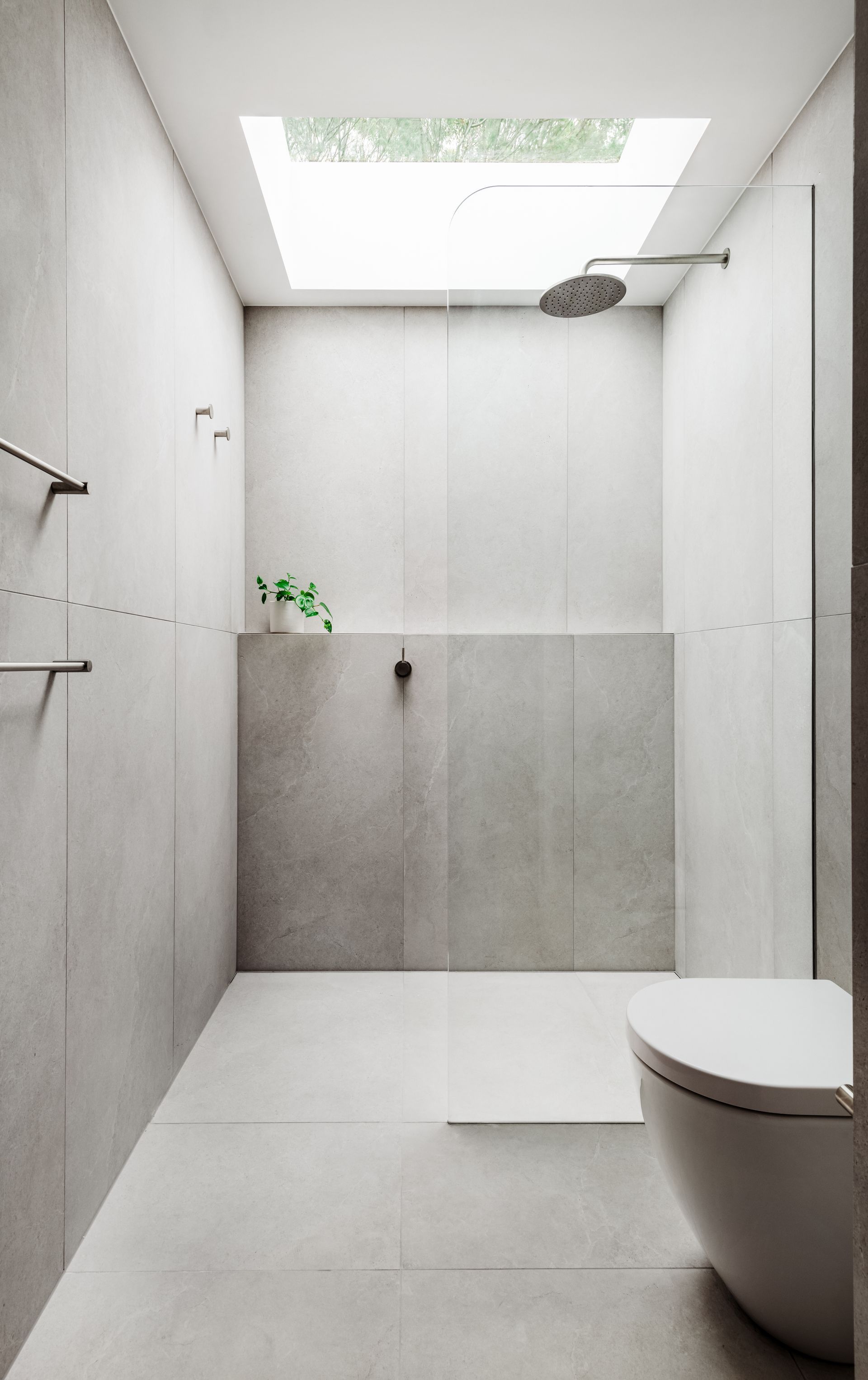 Modern white bathroom with skylight, shower, and toilet. Minimalist design with gray tiled walls — Escarpment Building in Austinmer, NSW