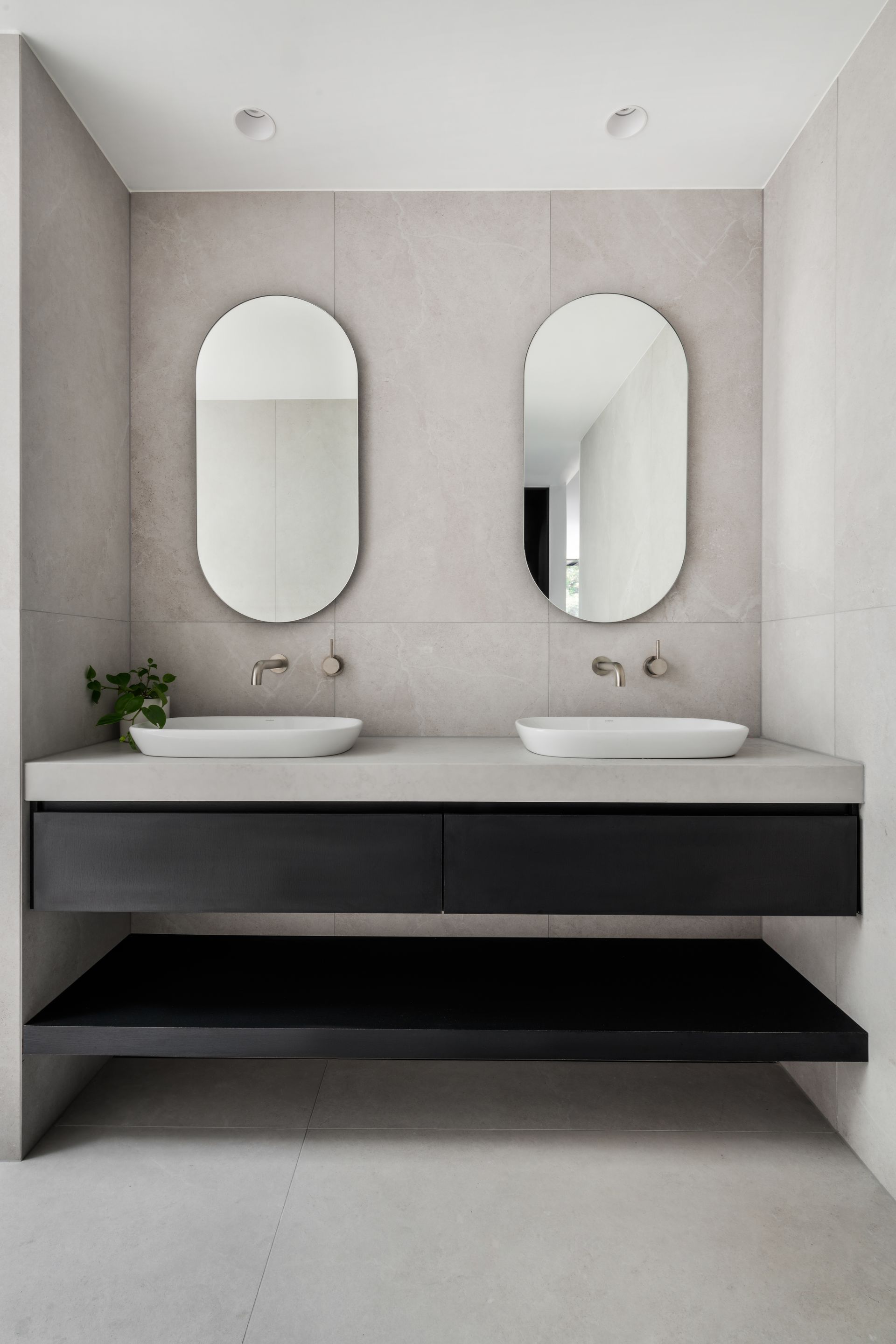 Modern bathroom with two sinks, oval mirrors, black floating vanity, and gray walls — Escarpment Building in Austinmer, NSW