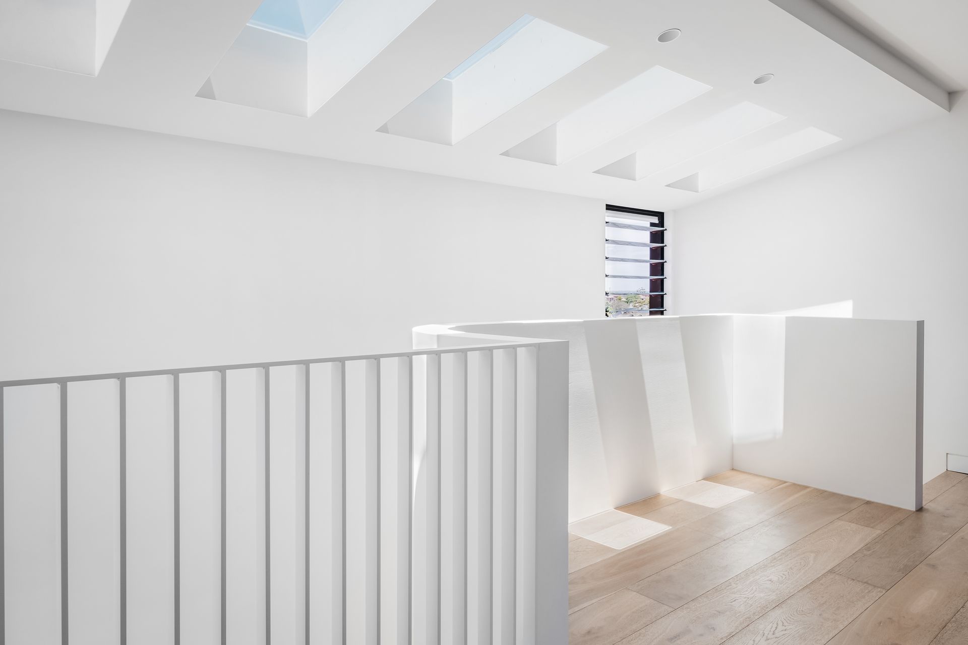 Bright white interior with angled walls, wooden floors, and skylights. A white railing is in the foreground — Escarpment Building in Austinmer, NSW