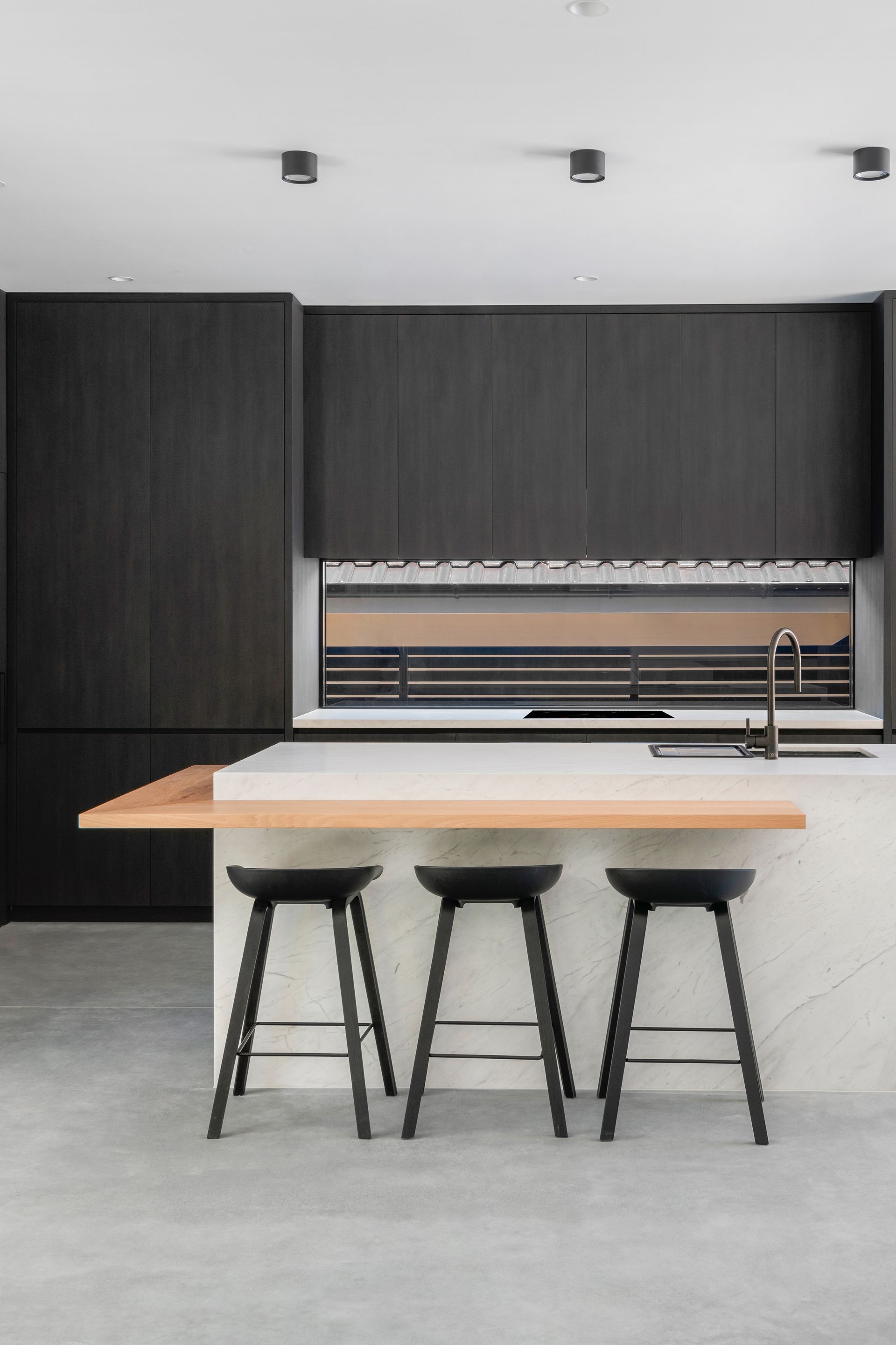 Modern kitchen with dark cabinetry, light countertop, and black stools at the island — Escarpment Building in Austinmer, NSW