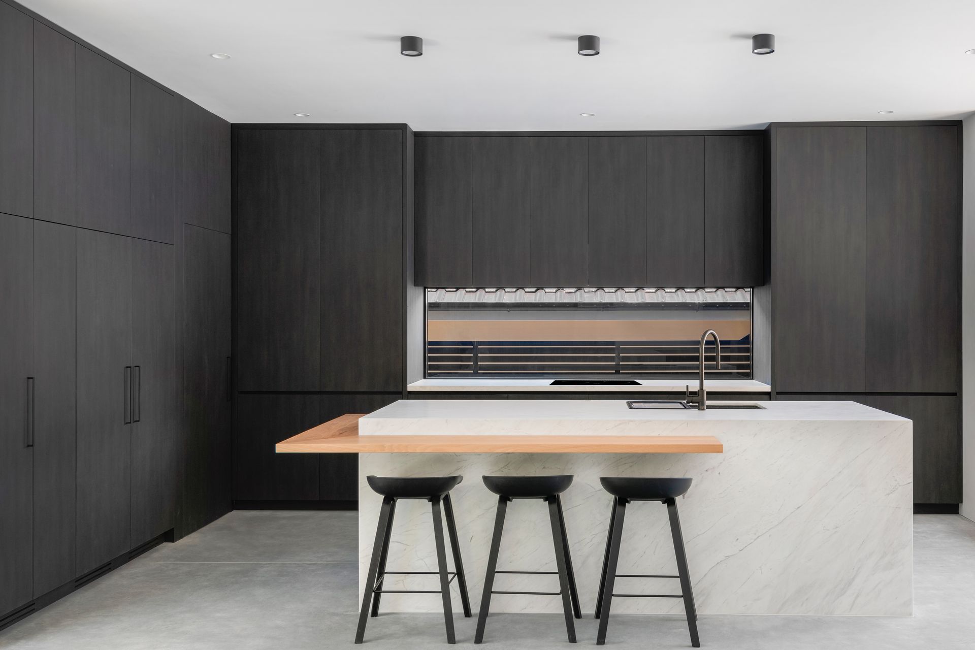 Modern kitchen with dark wood cabinets, white island, bar stools, and window