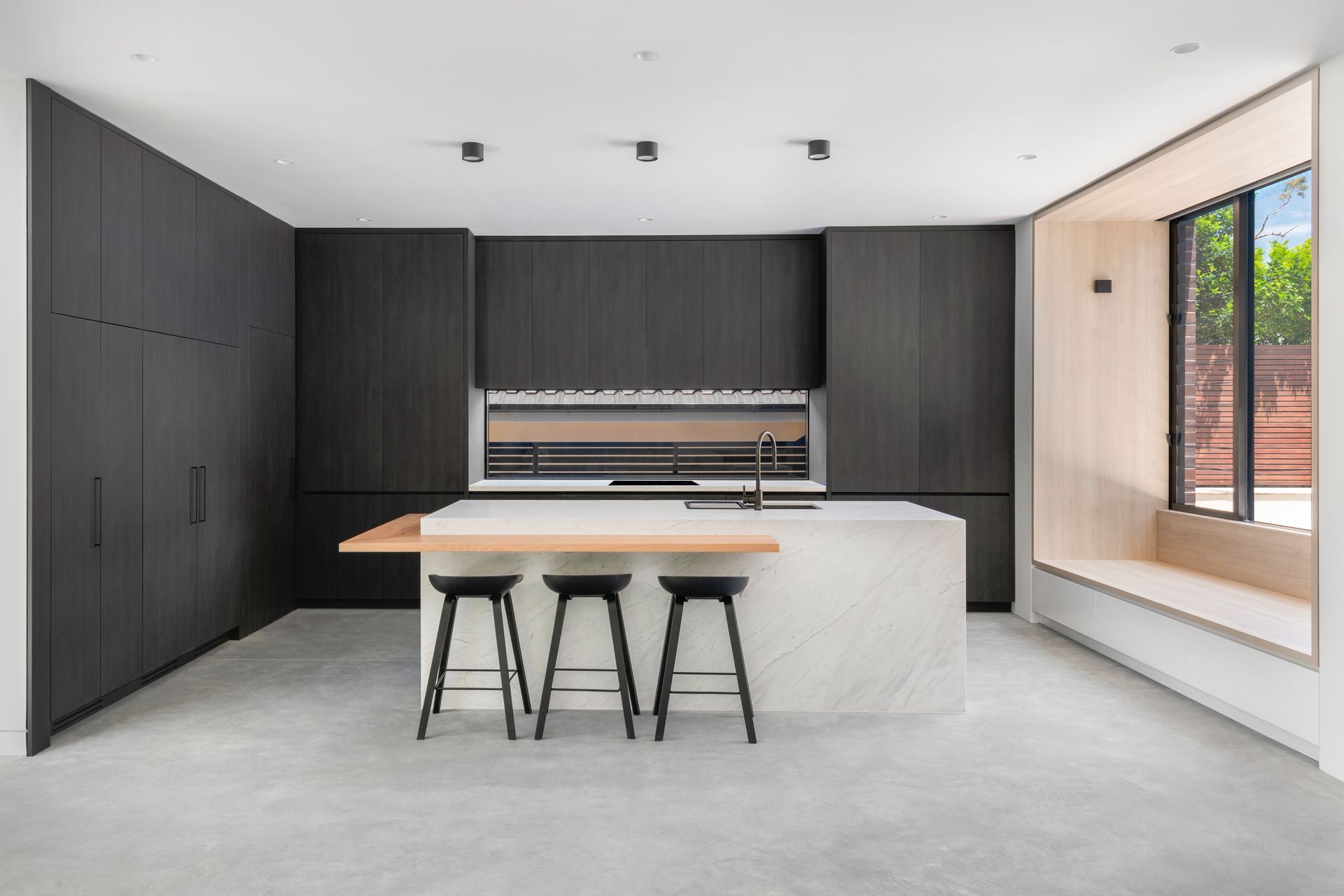 Modern kitchen with dark wood cabinets, a white island, and a light-filled window seat — Escarpment Building in Austinmer, NSW