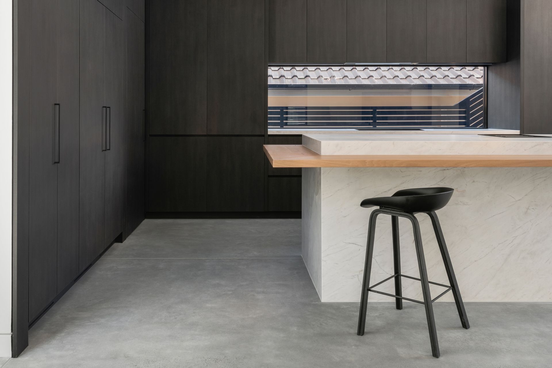Modern kitchen with dark wood cabinets, concrete floor, and light wood countertop, with a barstool — Escarpment Building in Austinmer, NSW