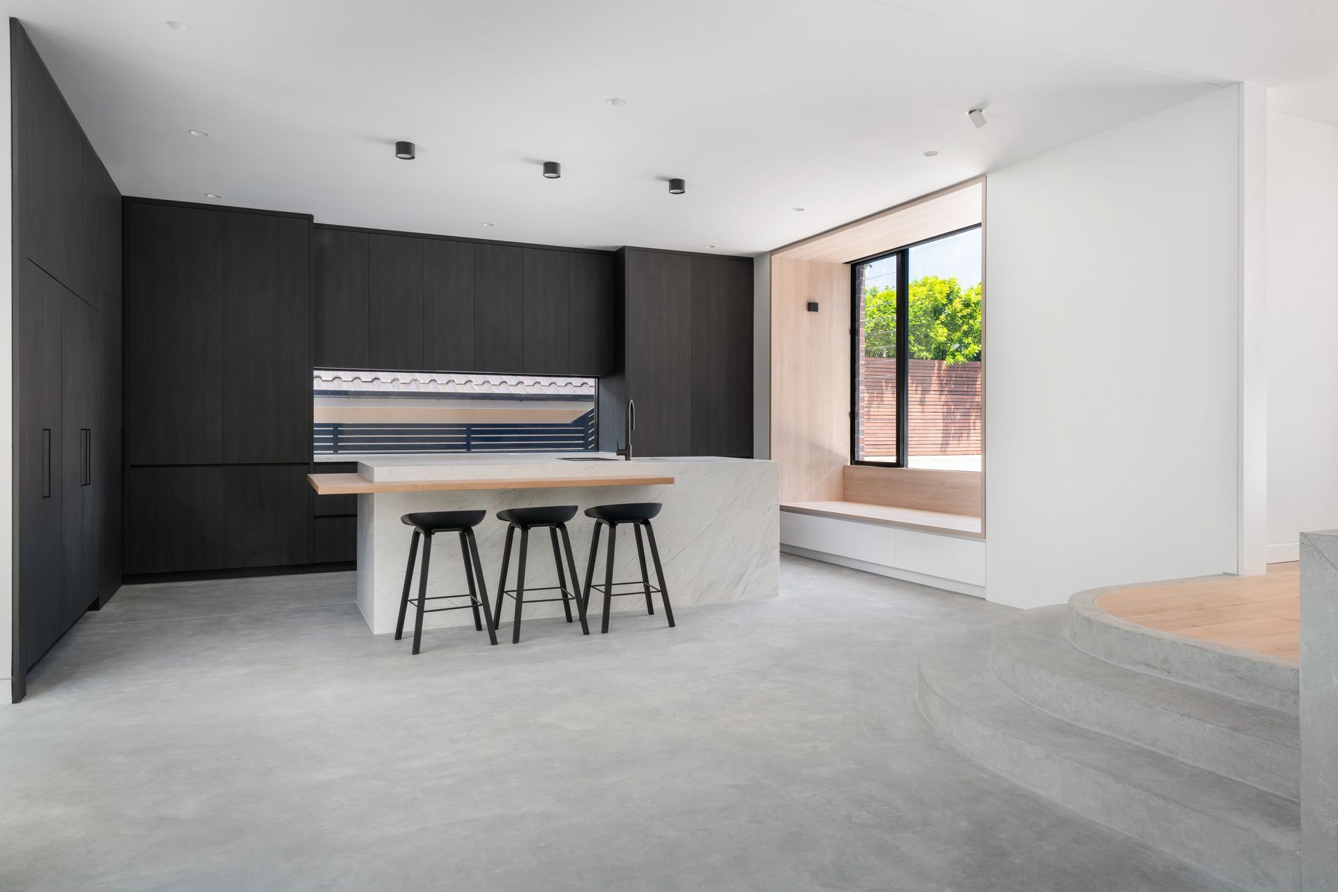 Modern kitchen with black cabinetry, white island with stools, and large window.