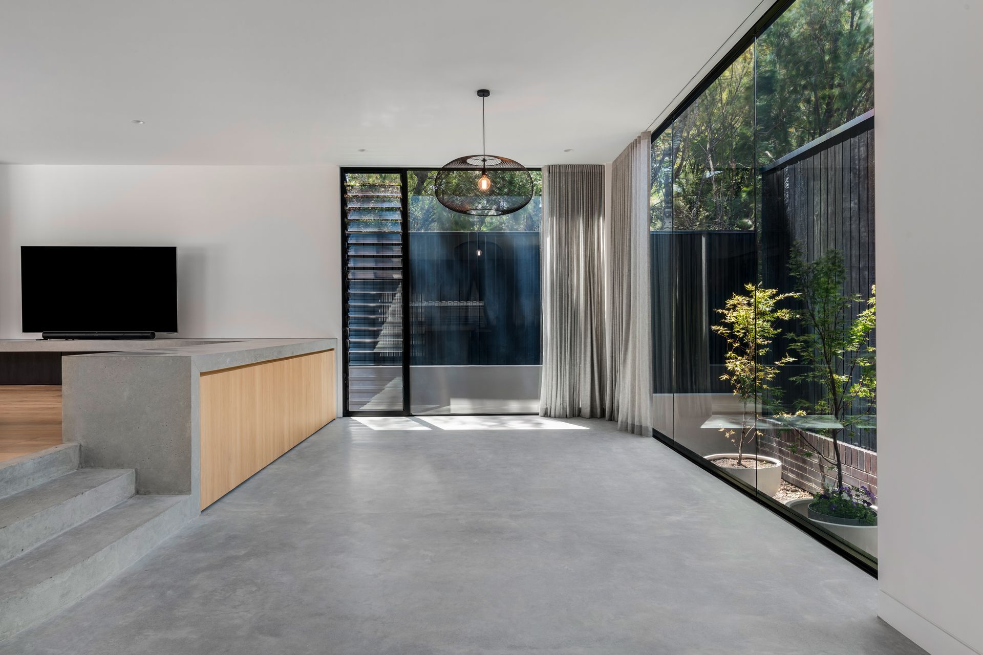 Modern interior with concrete floors, large windows overlooking a garden, and minimalist decor 