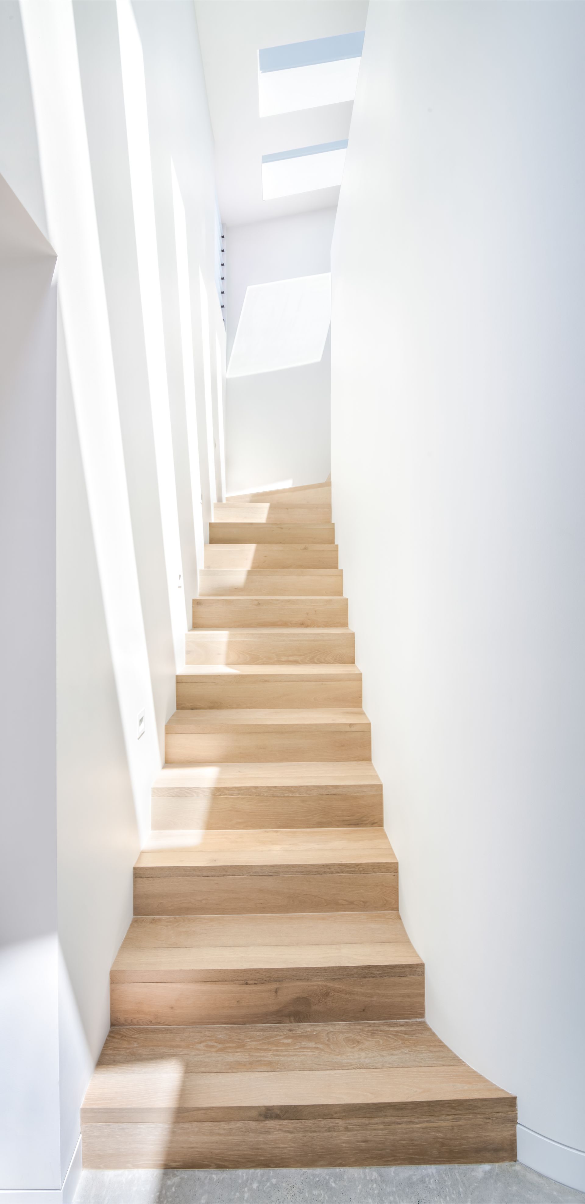 Wooden staircase in a white-walled hallway with sunlight streaming in from above — Escarpment Building in Austinmer, NSW