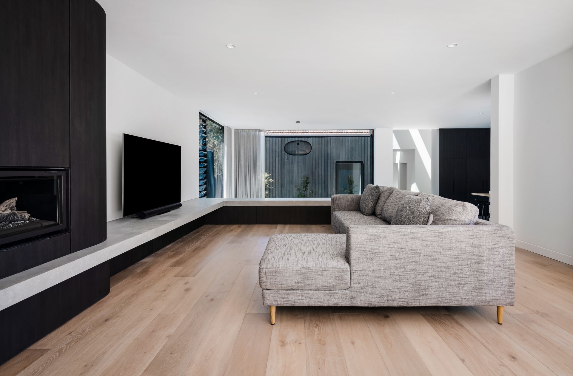 Modern living room with fireplace, TV, and gray sectional sofa on light wood floors — Escarpment Building in Austinmer, NSW