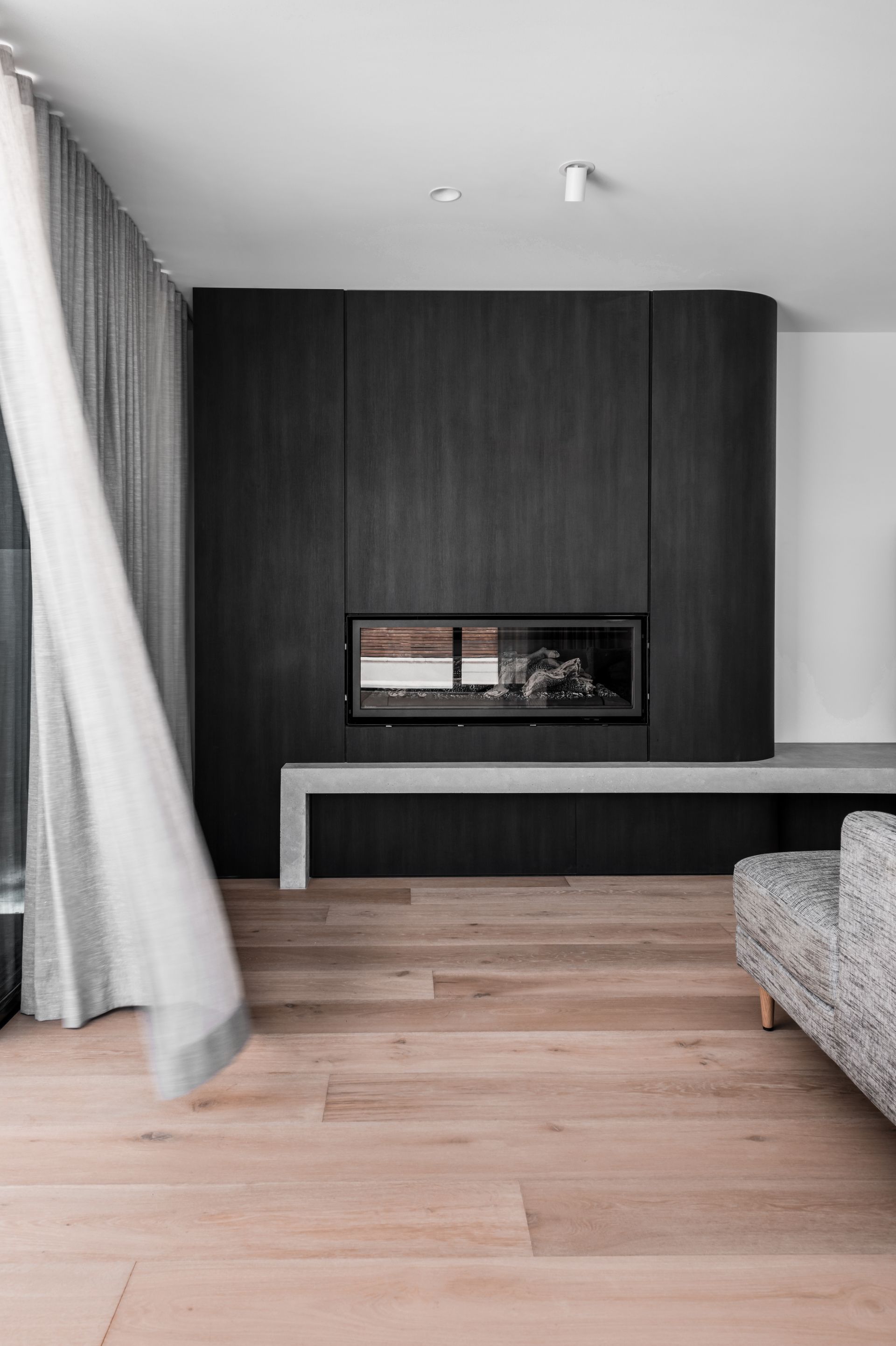 Modern living room with dark wood fireplace wall, light wood floor, and sheer curtains — Escarpment Building in Austinmer, NSW