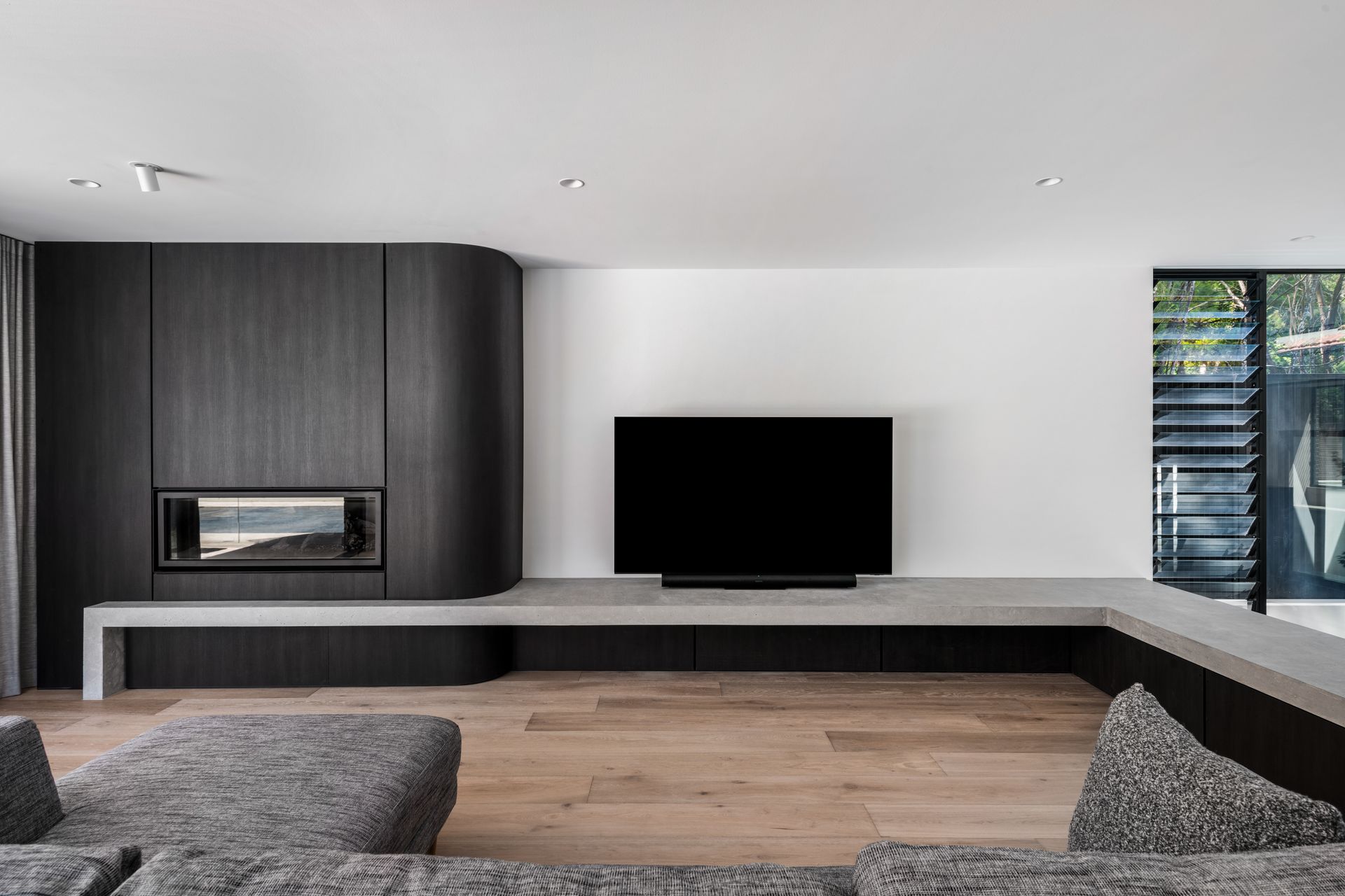 Modern living room with a built-in fireplace and TV on a gray platform — Escarpment Building in Austinmer, NSW