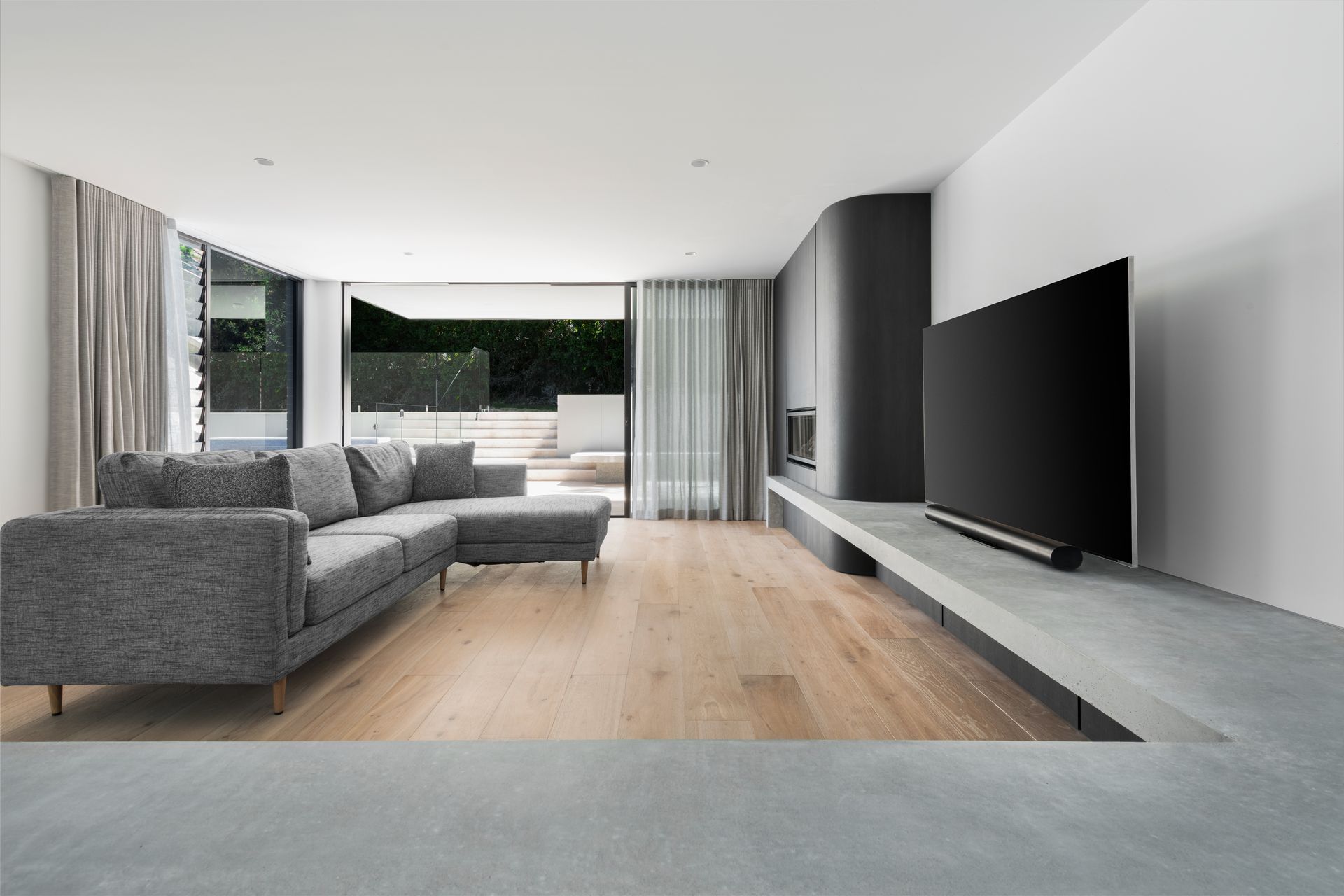 Modern living room with grey sectional, large TV, and open doors to patio — Escarpment Building in Austinmer, NSW
