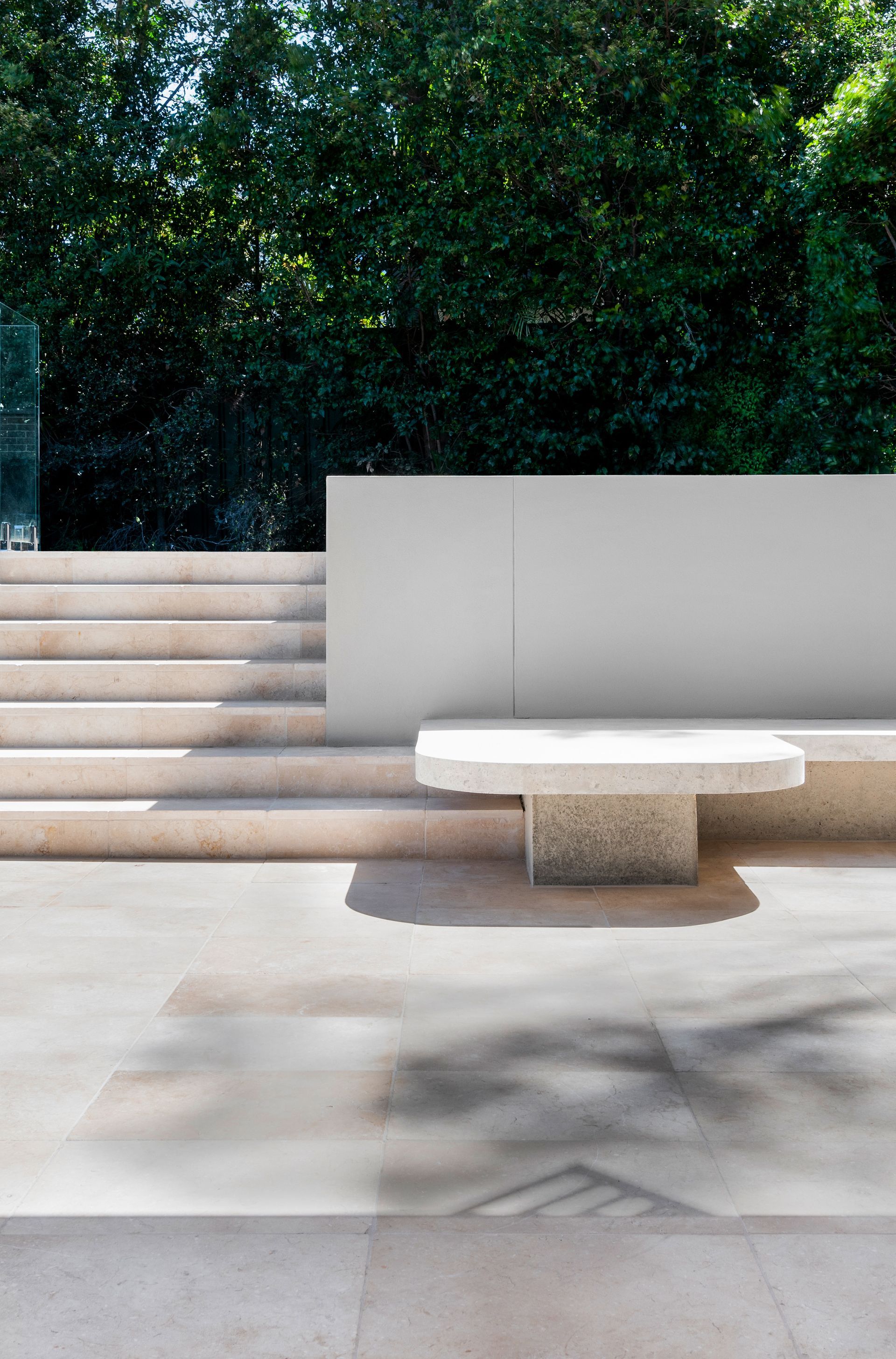 Stone patio with built-in bench, stairs, and a wall against lush green trees. Sunny outdoor setting — Escarpment Building in Austinmer, NSW