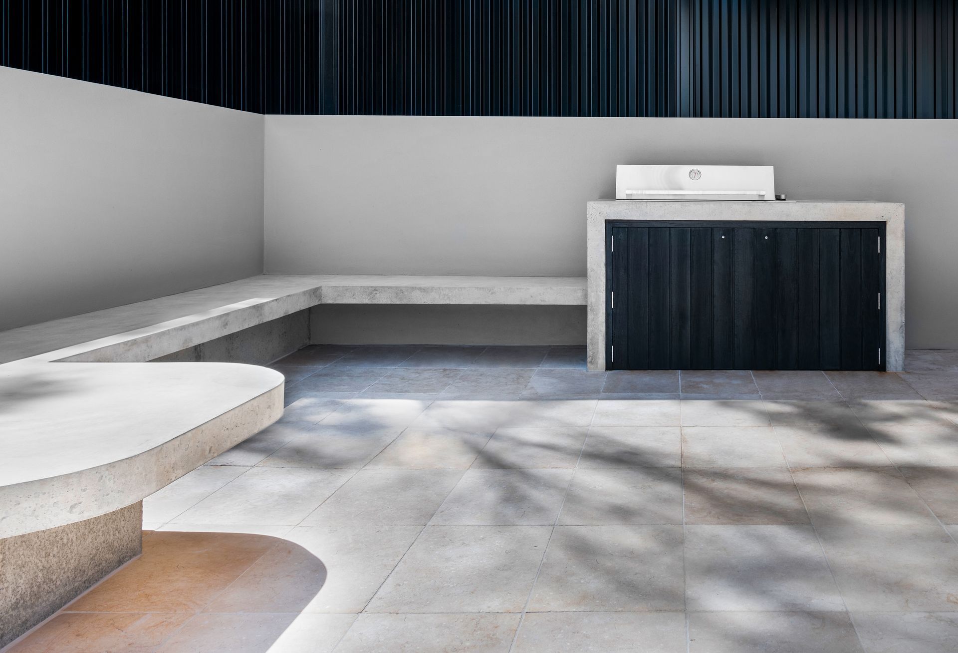 Outdoor seating area with concrete bench and counter, dark wood cabinet, and stone flooring — Escarpment Building in Austinmer, NSW