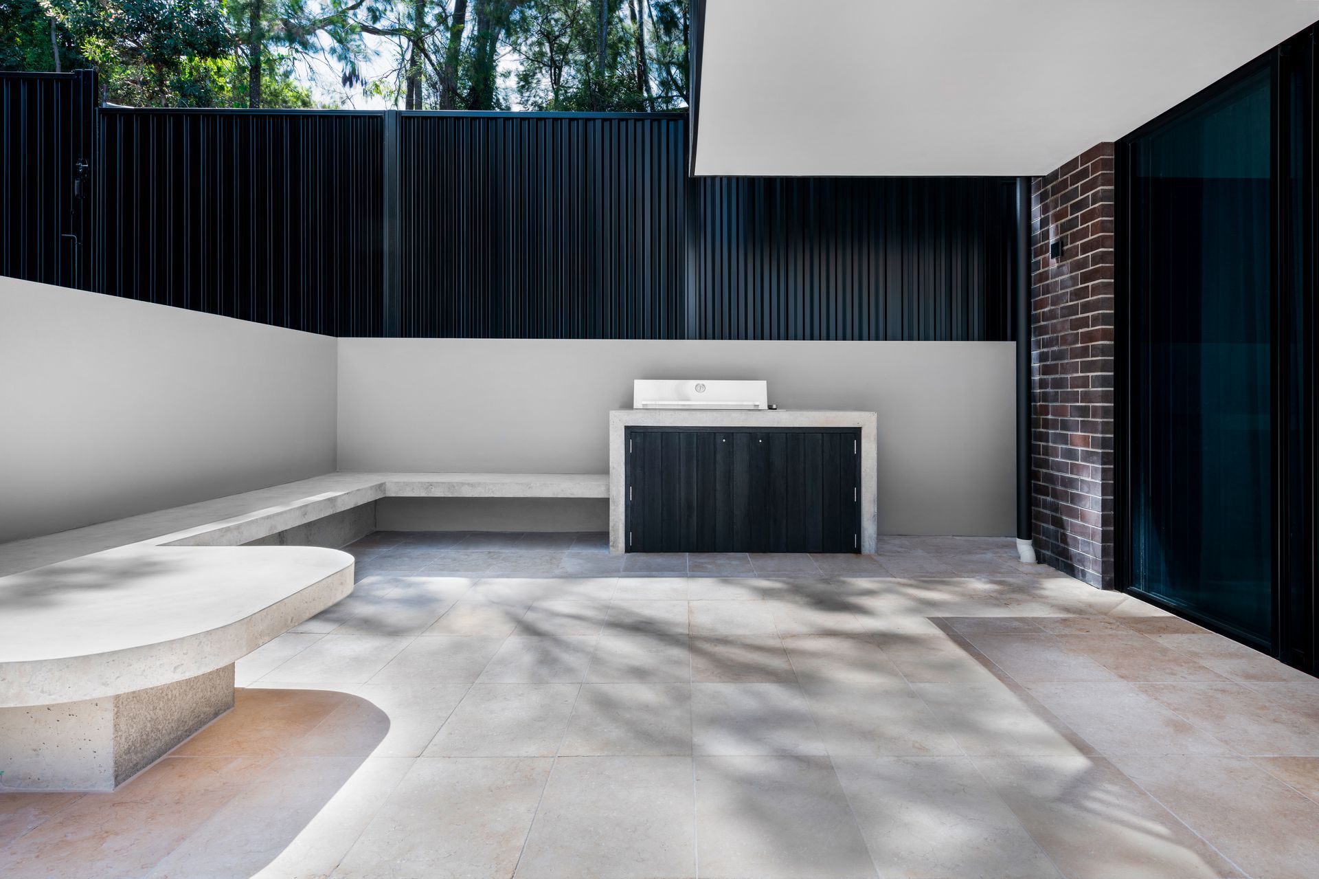 Outdoor patio with built-in seating, a grill station, and corrugated black fence — Escarpment Building in Austinmer, NSW
