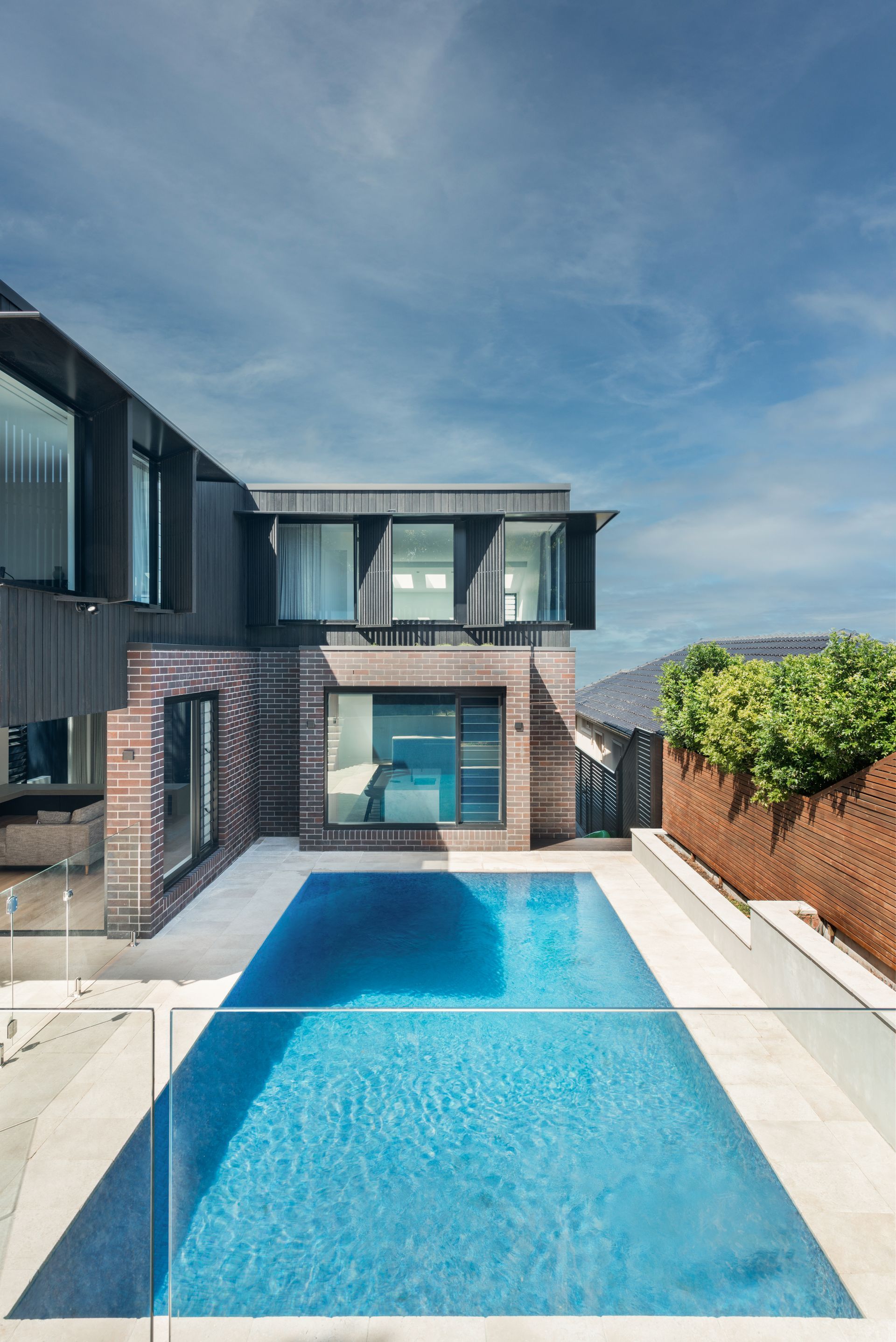 Modern house with swimming pool, blue water reflecting the sky. Exterior view under a bright sky.