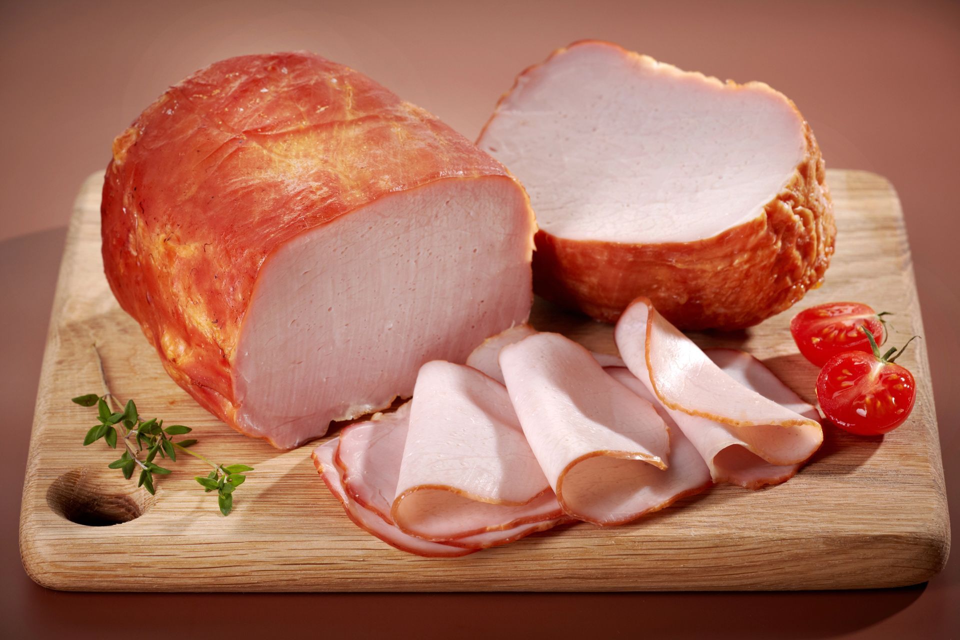 Pastel de carne ahumado y fiambres en rodajas sobre una tabla de cortar de madera con tomates y hierbas.