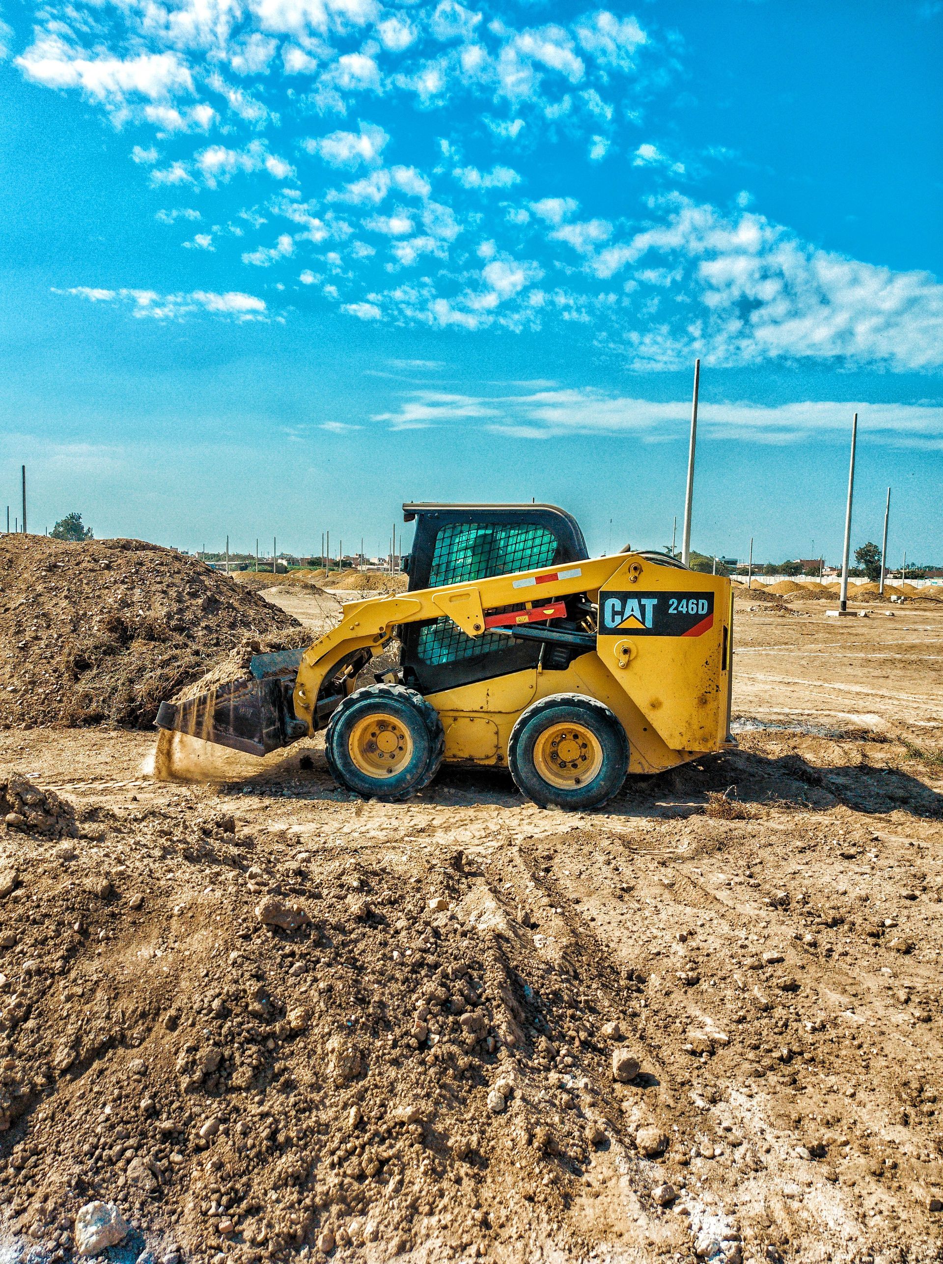 Yellow skid steer loader moving dirt at a construction site under a bright blue sky