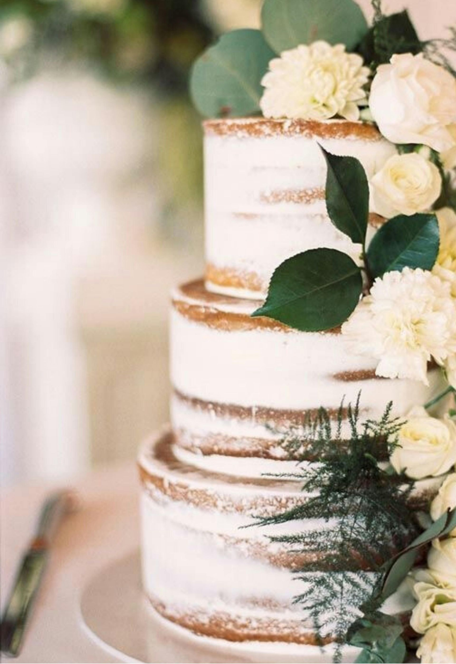Two-tier white wedding cake with gold accents and white flowers and greenery