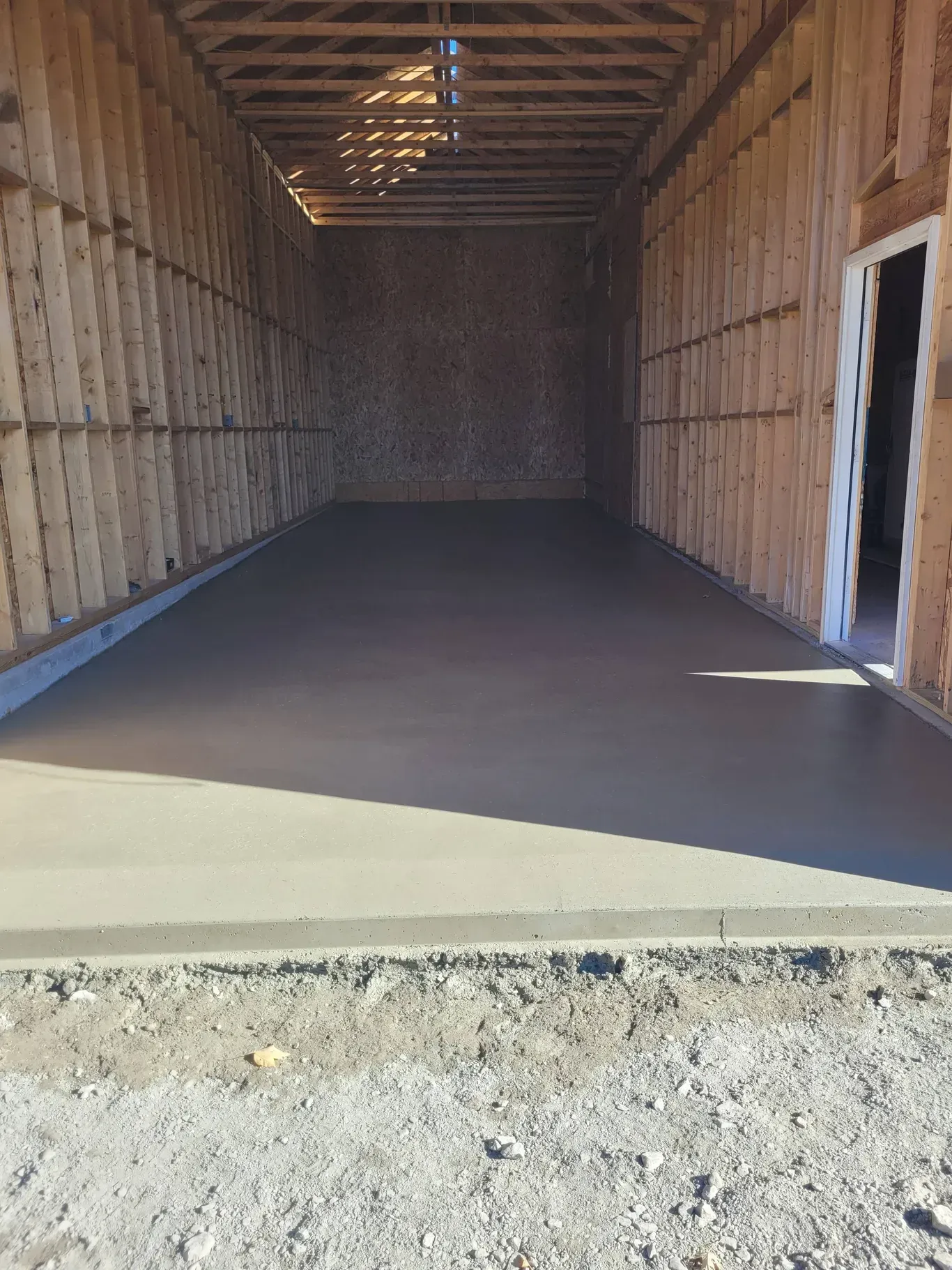 A newly poured concrete floor inside a wooden-framed structure under construction, with a doorway on the right.