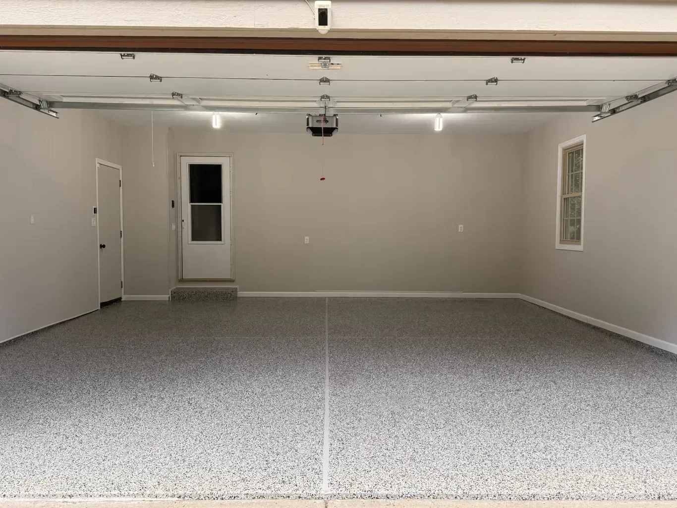 A spacious, empty two-car garage with a gray and white speckled epoxy floor, light walls, and two white doors.