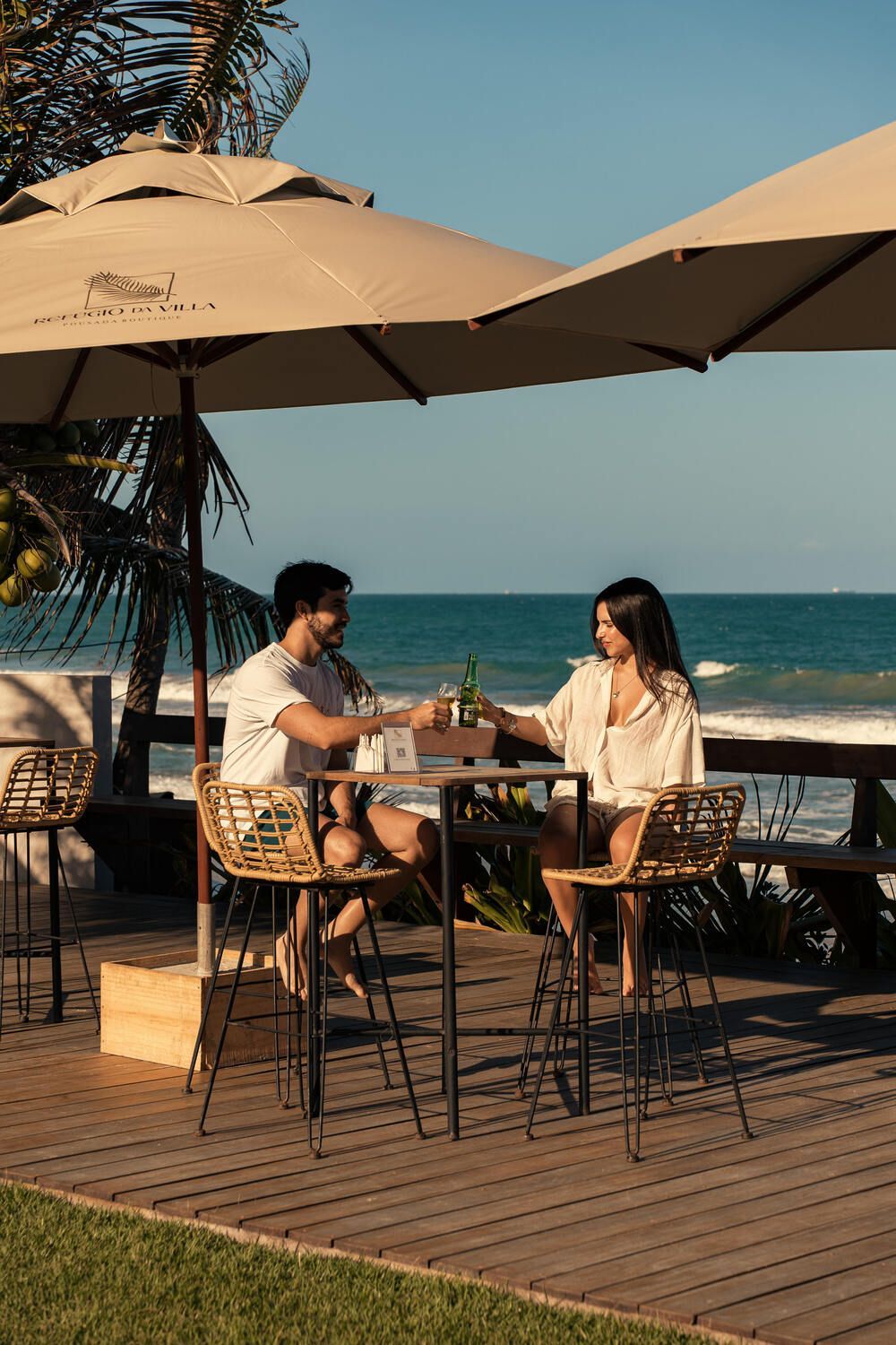 Um homem e uma mulher estão sentados à mesa sob guarda-sóis perto do oceano.