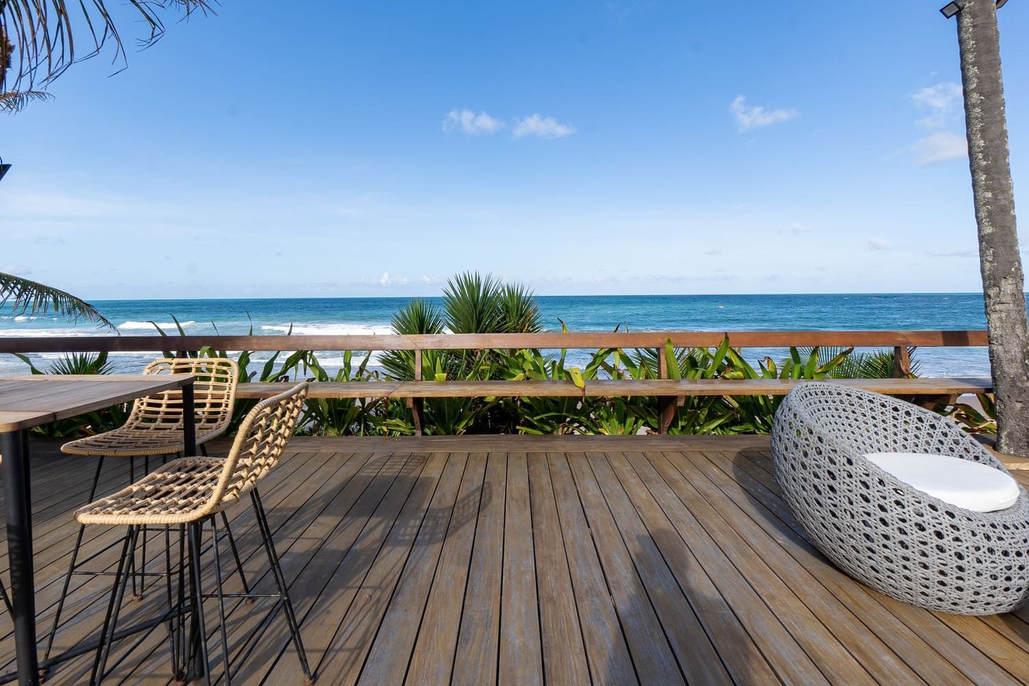 Um deck de madeira com cadeiras e uma mesa com vista para o oceano.