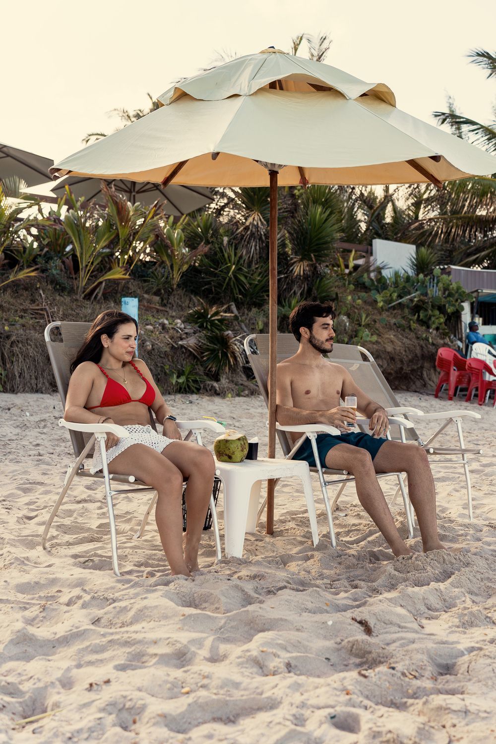 Um homem e uma mulher estão sentados sob um guarda-sol na praia.
