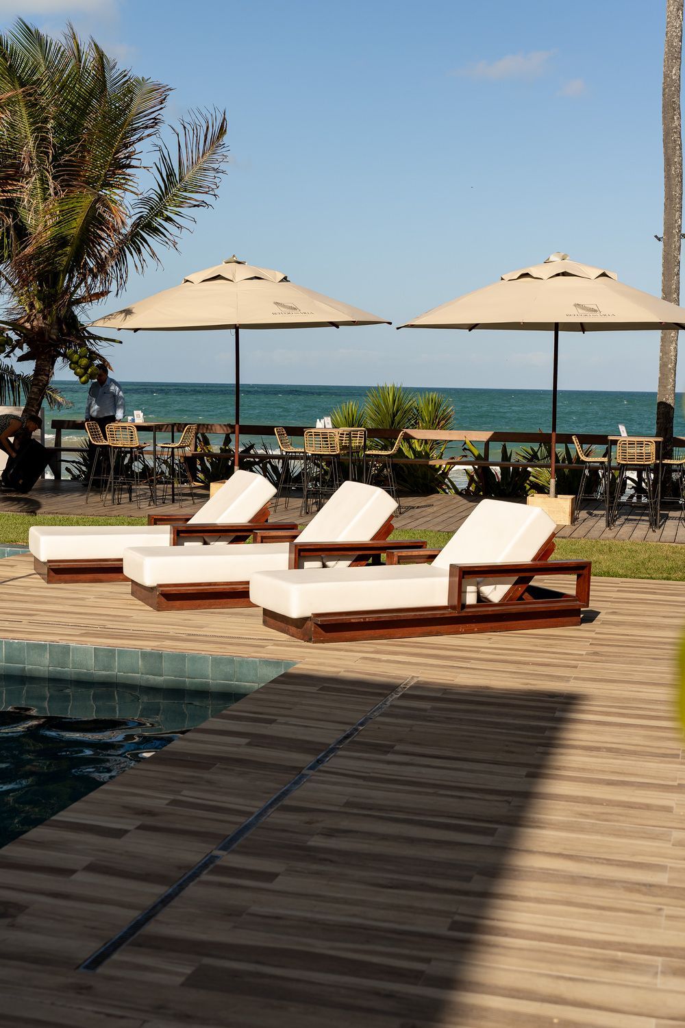 Uma fileira de espreguiçadeiras e guarda-sóis em um deck com vista para o oceano.