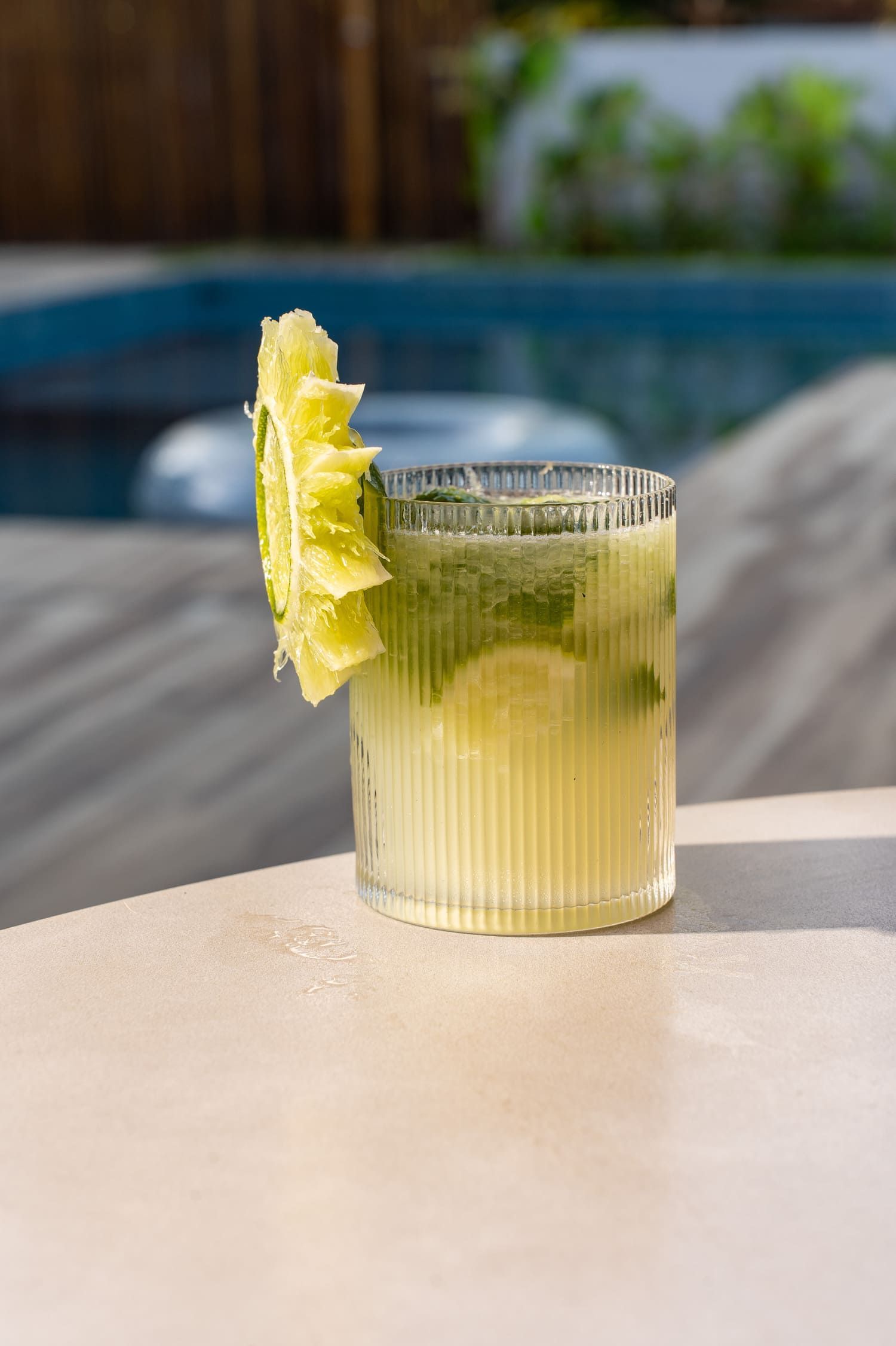 Um close de uma bebida em uma mesa ao lado de uma piscina.