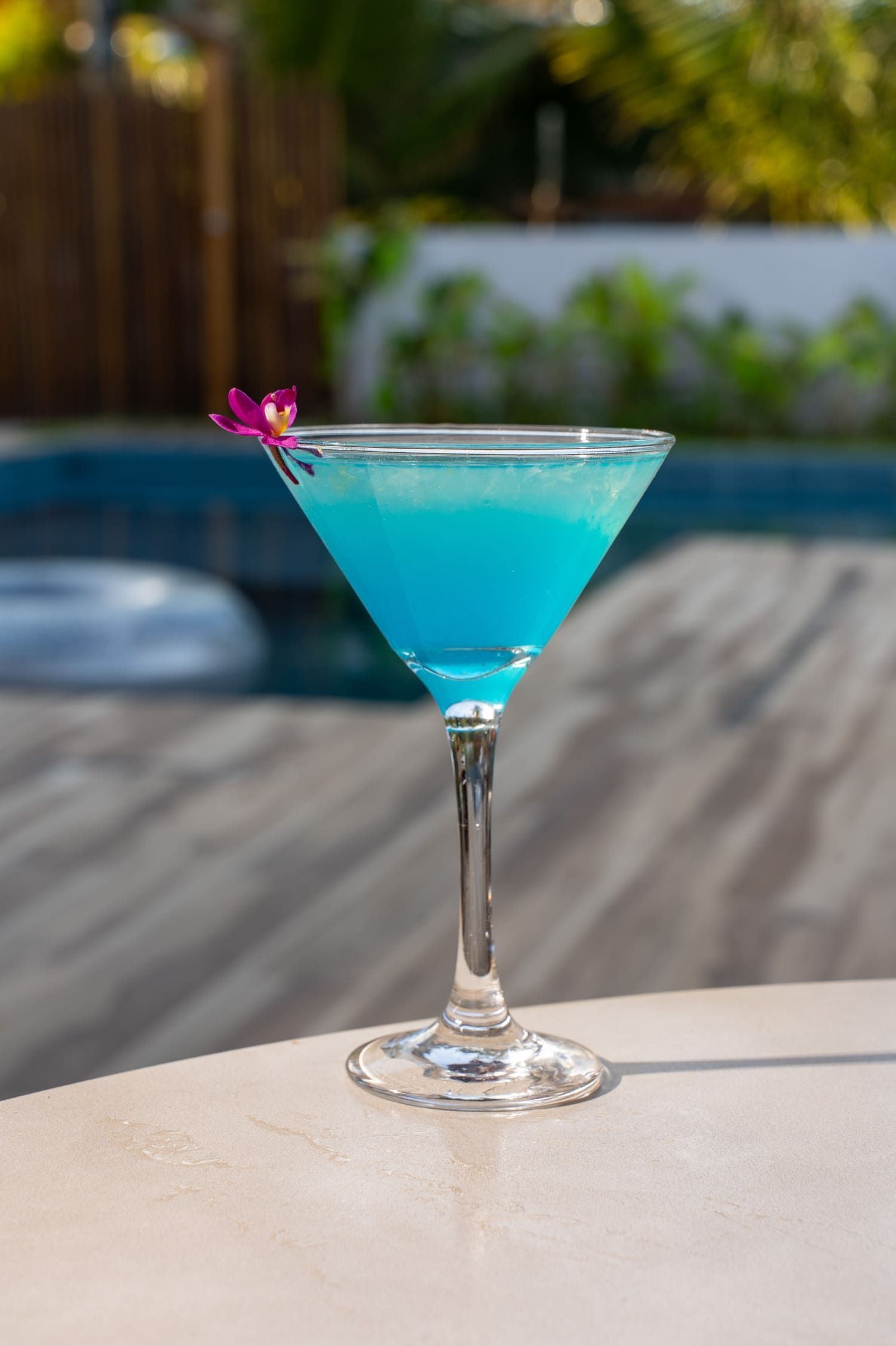 Um martini azul está sobre uma mesa ao lado de uma piscina.
