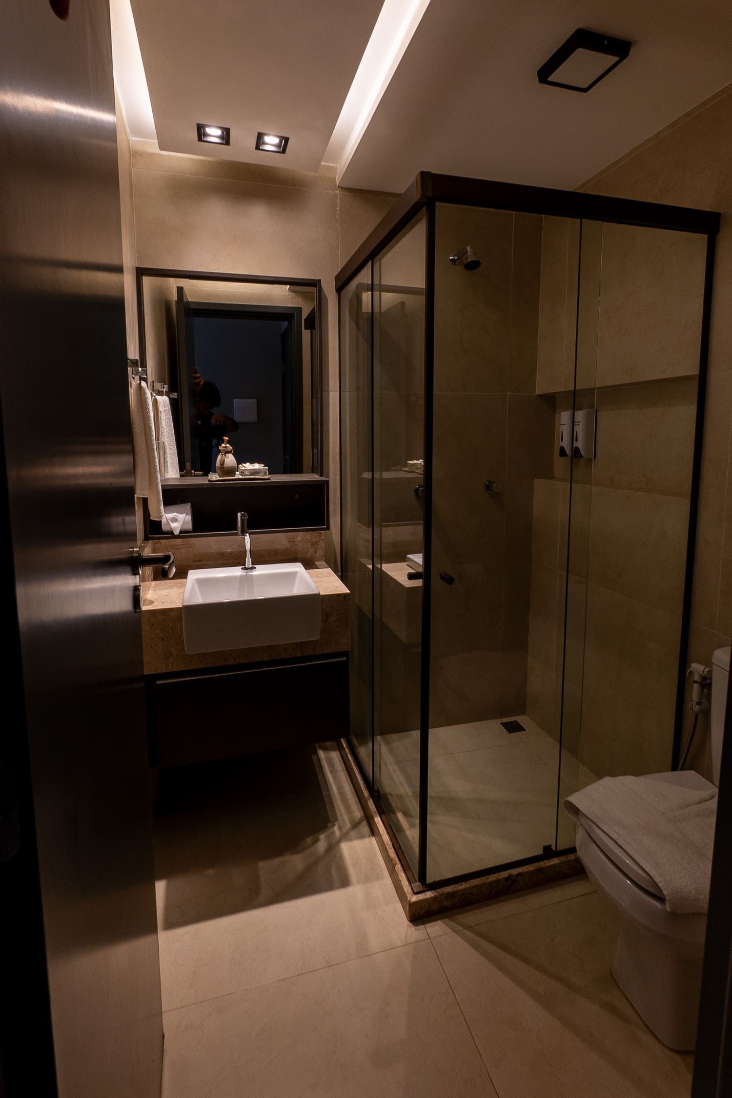 Um banheiro com vaso sanitário, pia, chuveiro e espelho.