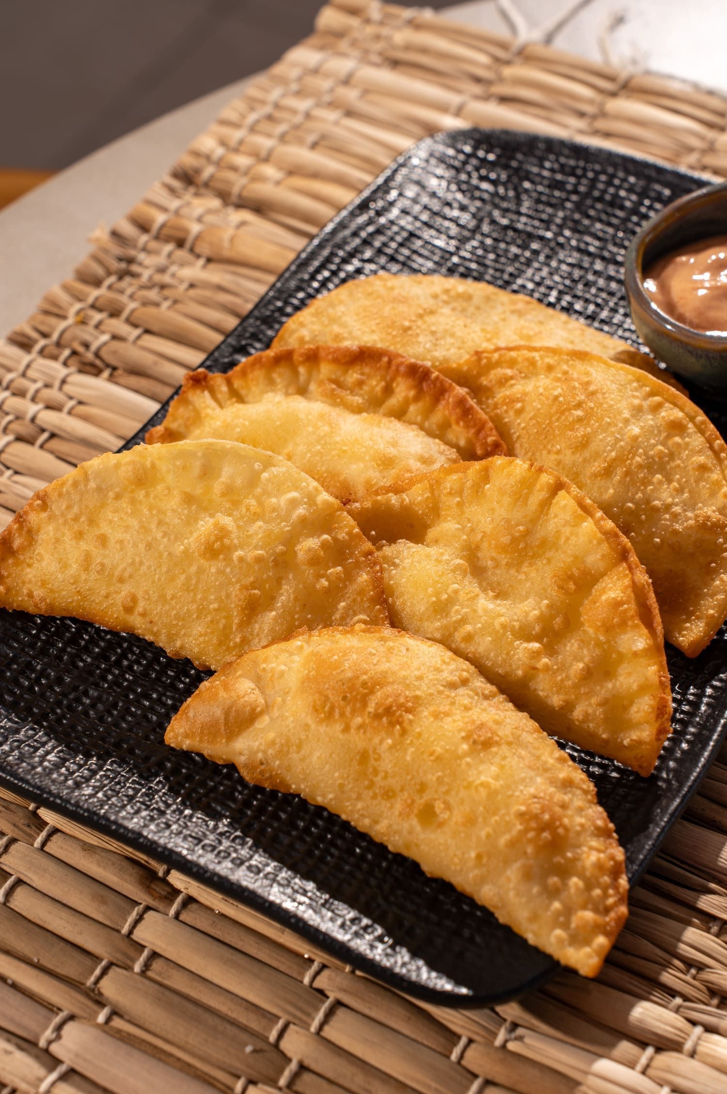 Um prato preto coberto com pastéis fritos e uma tigela de molho.