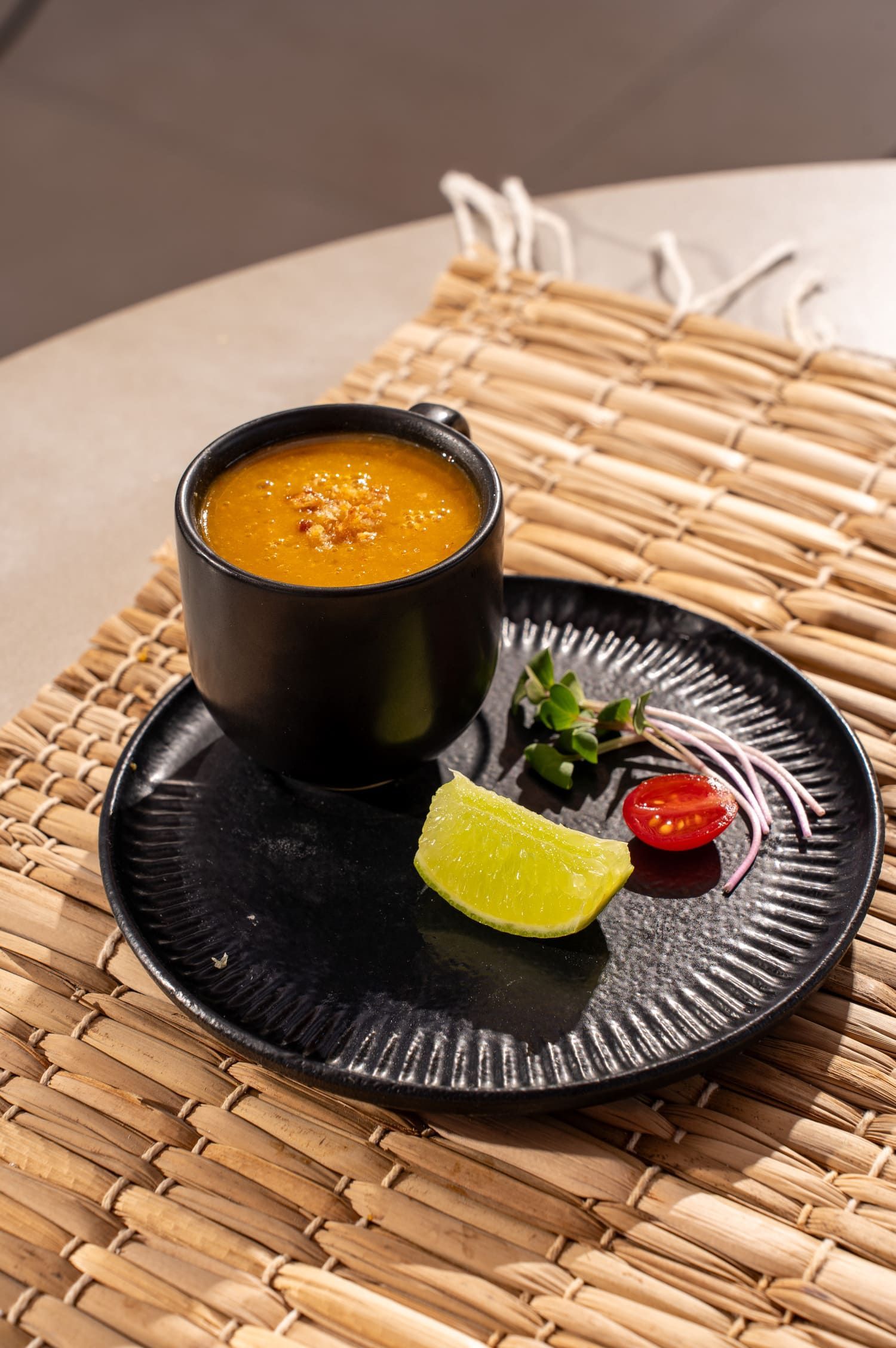 Uma xícara de sopa está sobre um prato preto sobre uma mesa.