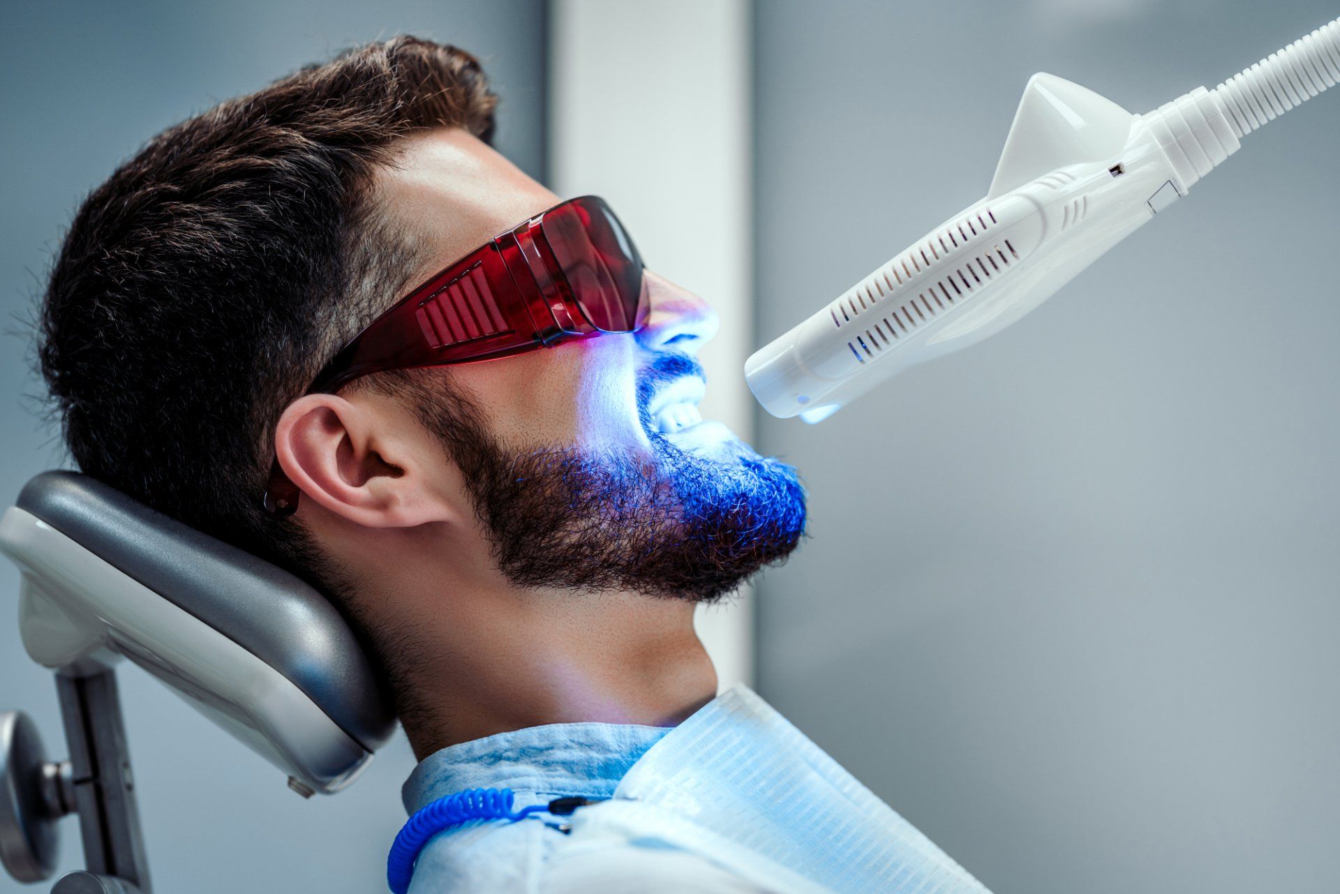 man receiving teeth whitening treatment under blue light