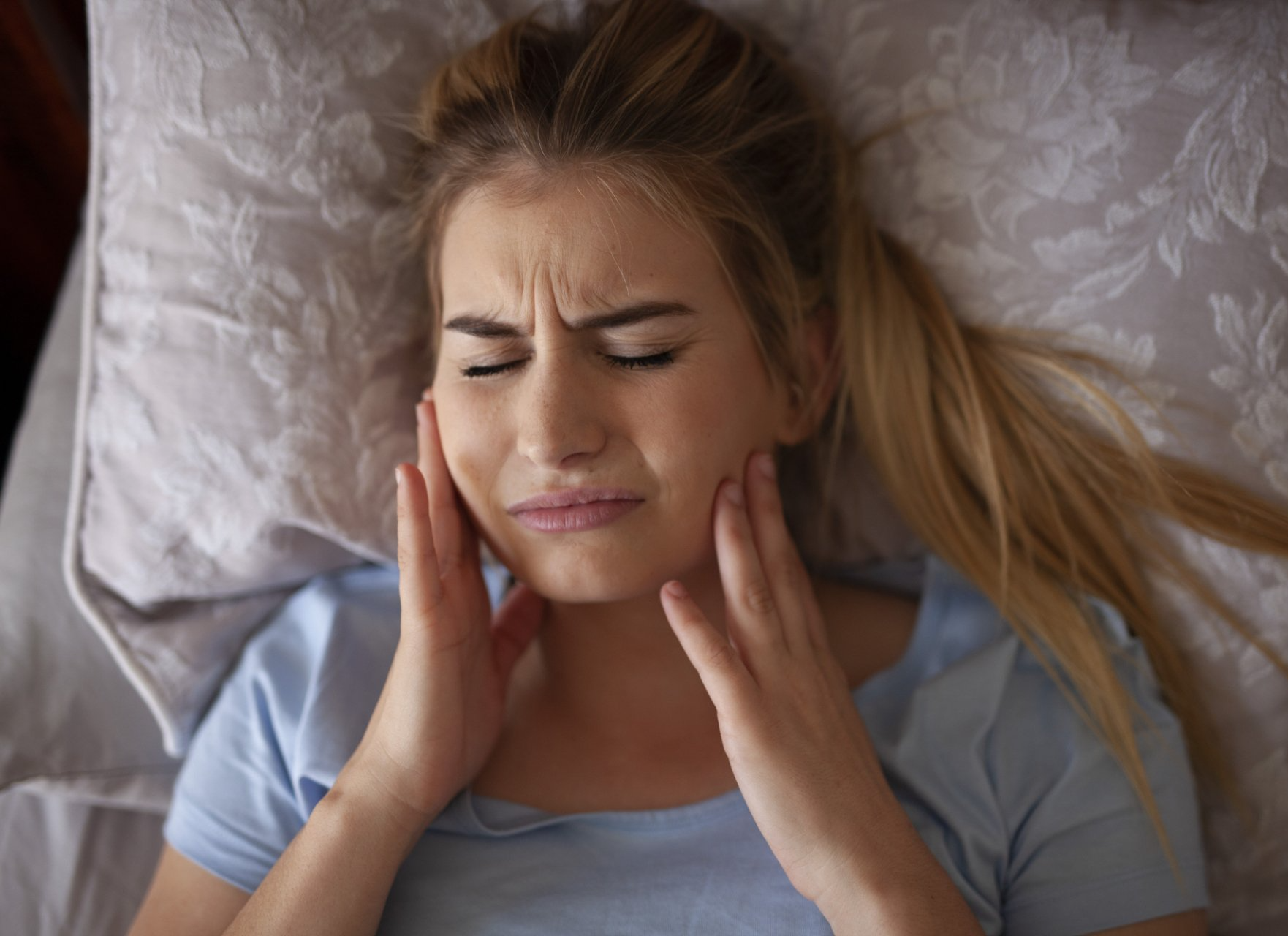 young woman has TMJ jaw pain after sleeping
