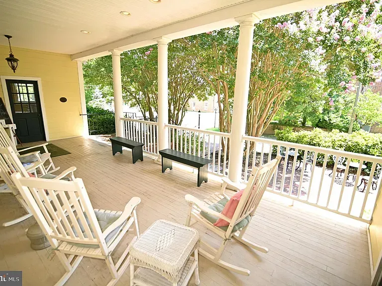 Covered porch with white columns, rocking chairs, and small benches.