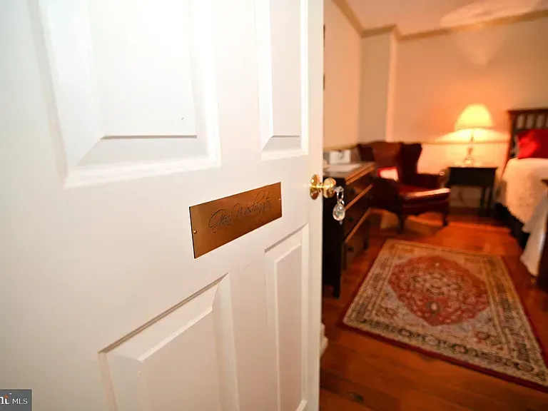 White door slightly ajar revealing a bedroom with a bed, desk, and area rug.