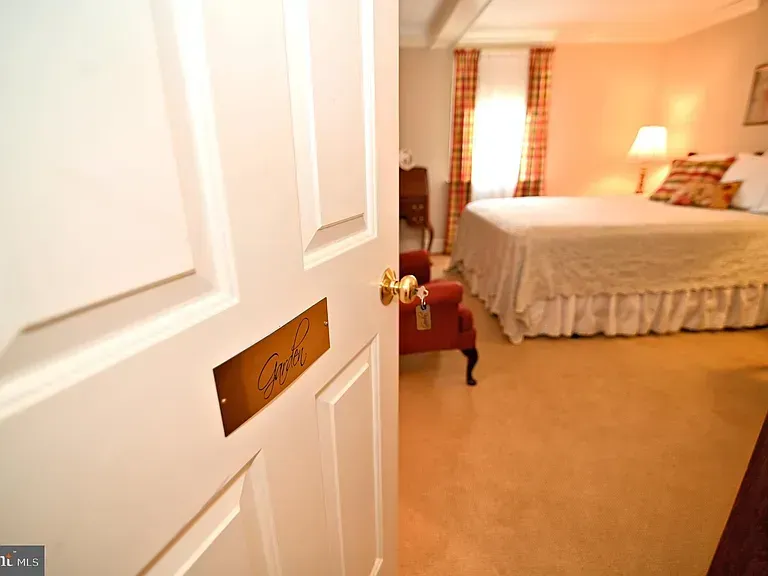 Open white door to a bedroom with bed, chair, and window. Room nameplate reads "Carl."