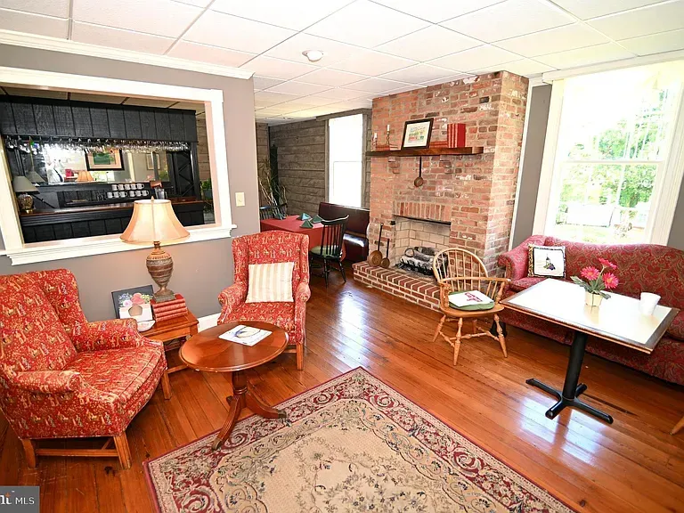 Living room with red patterned furniture, brick fireplace, and hardwood floors.