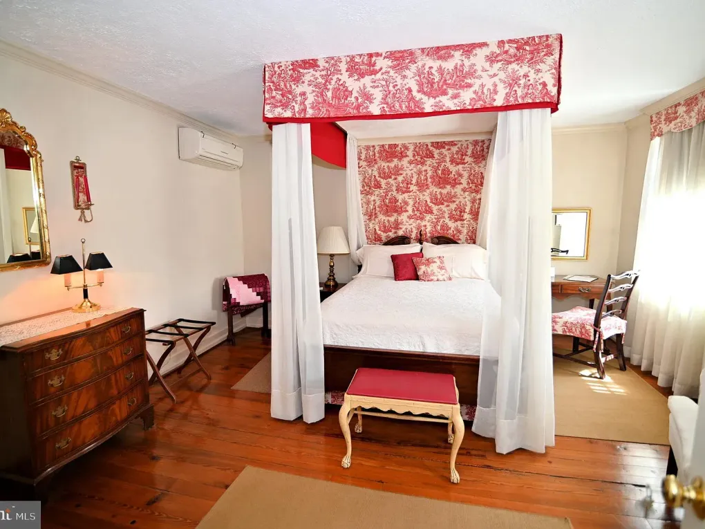 Bedroom with canopy bed, red toile wallpaper and accents, hardwood floor.