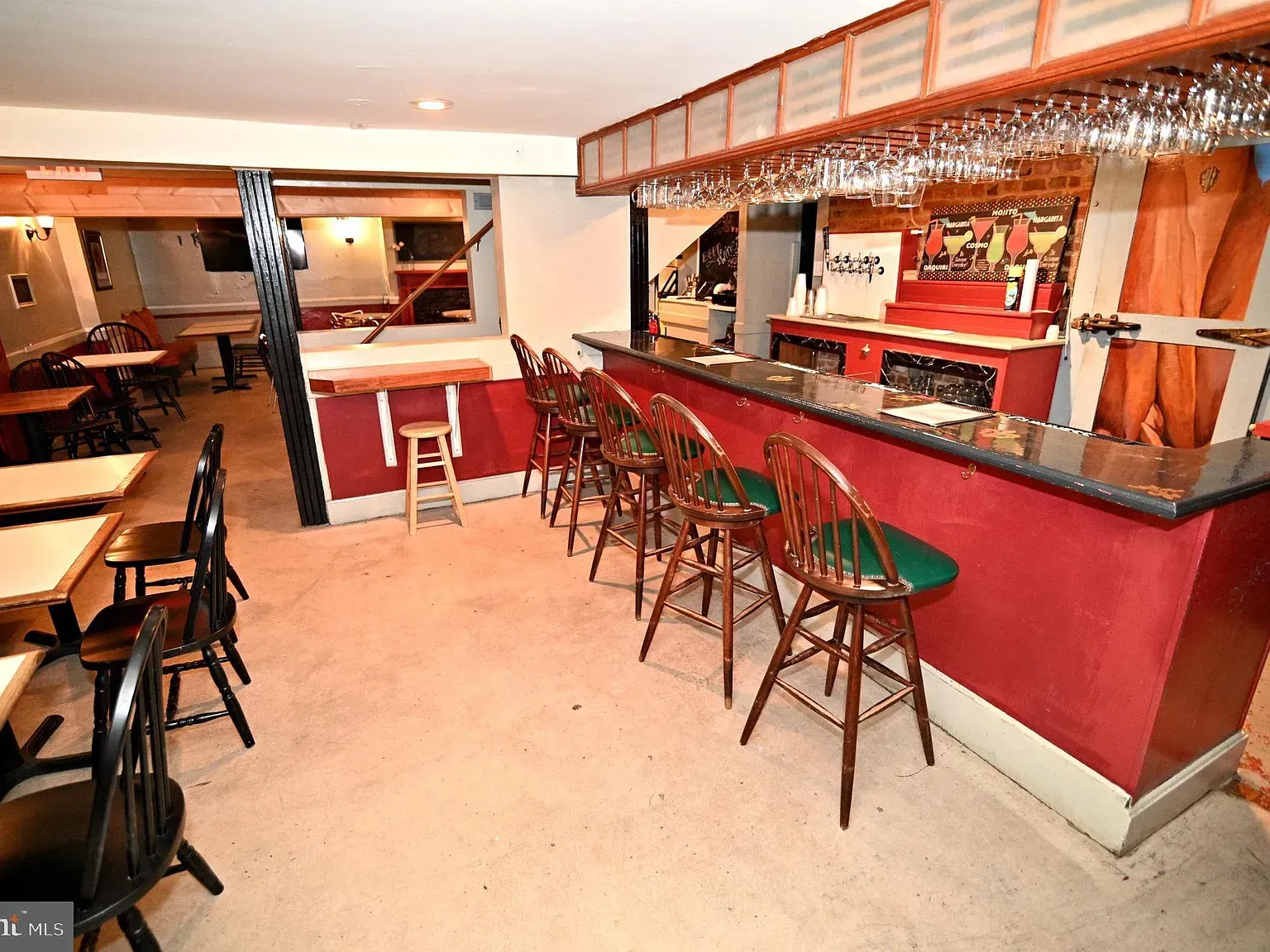 Interior of a bar with a red counter, bar stools, tables, and glassware hanging above.